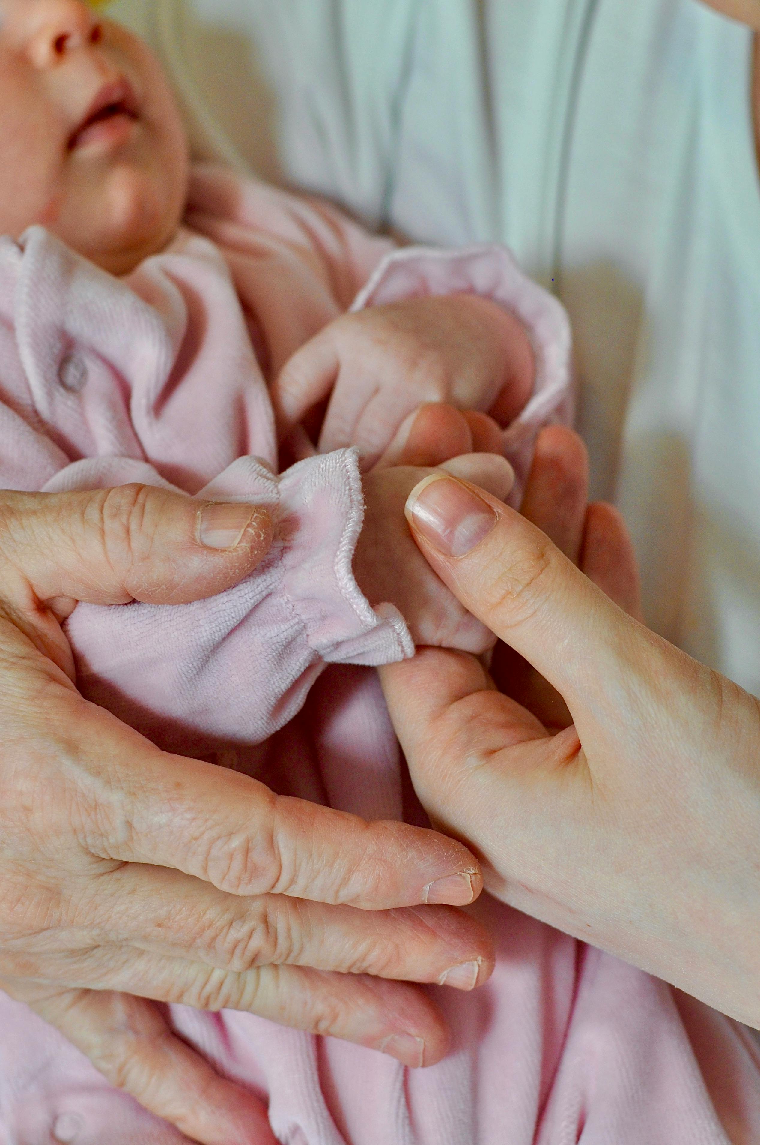 Close-up of senior and adult hands holding a baby, reflecting family connection.