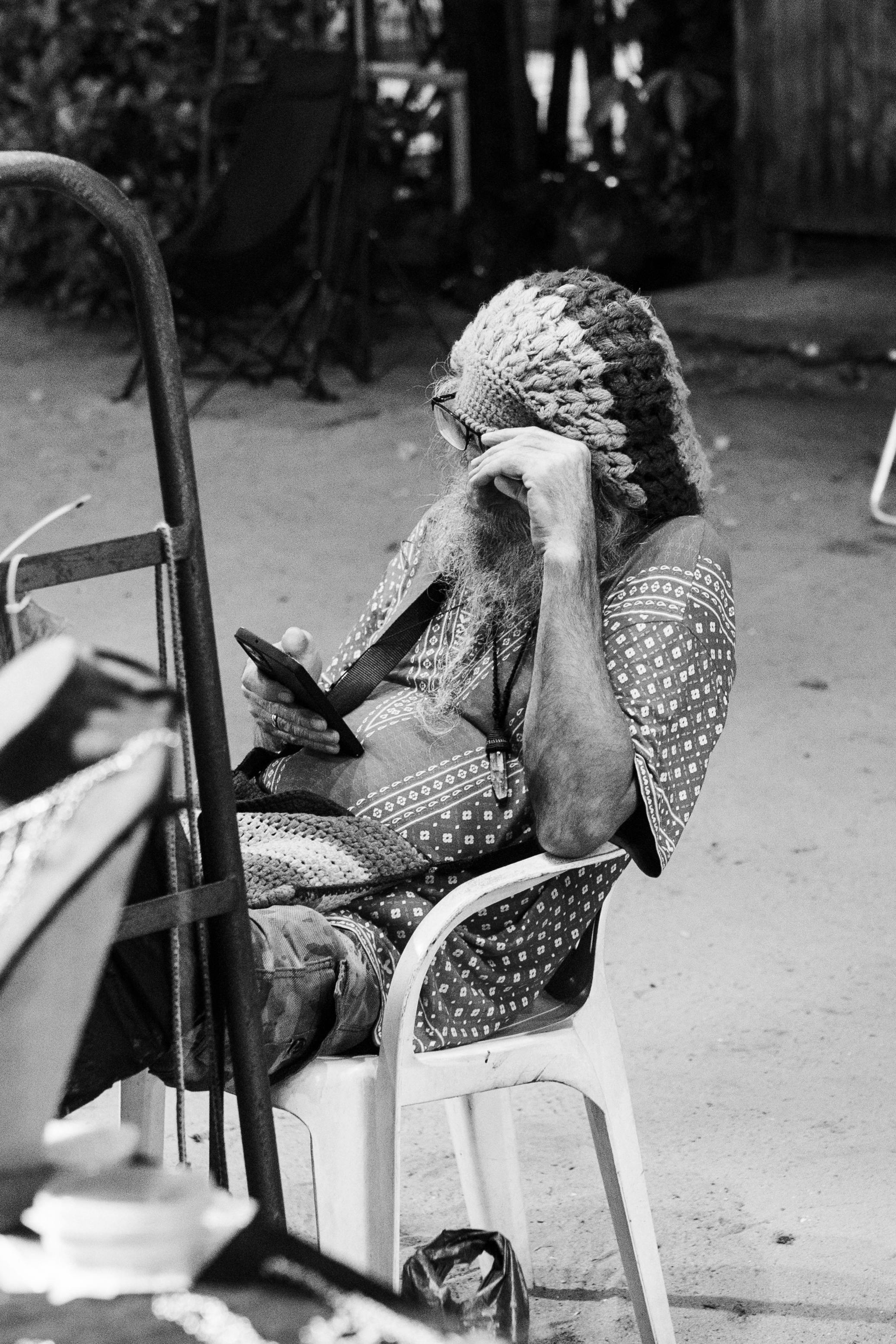 Безкоштовне Чоловік відпочиває на свіжому повітрі, користуючись мобільним телефоном, у візерунчастій сорочці та в'язаній шапці. Чорно-біле зображення. стокове фото