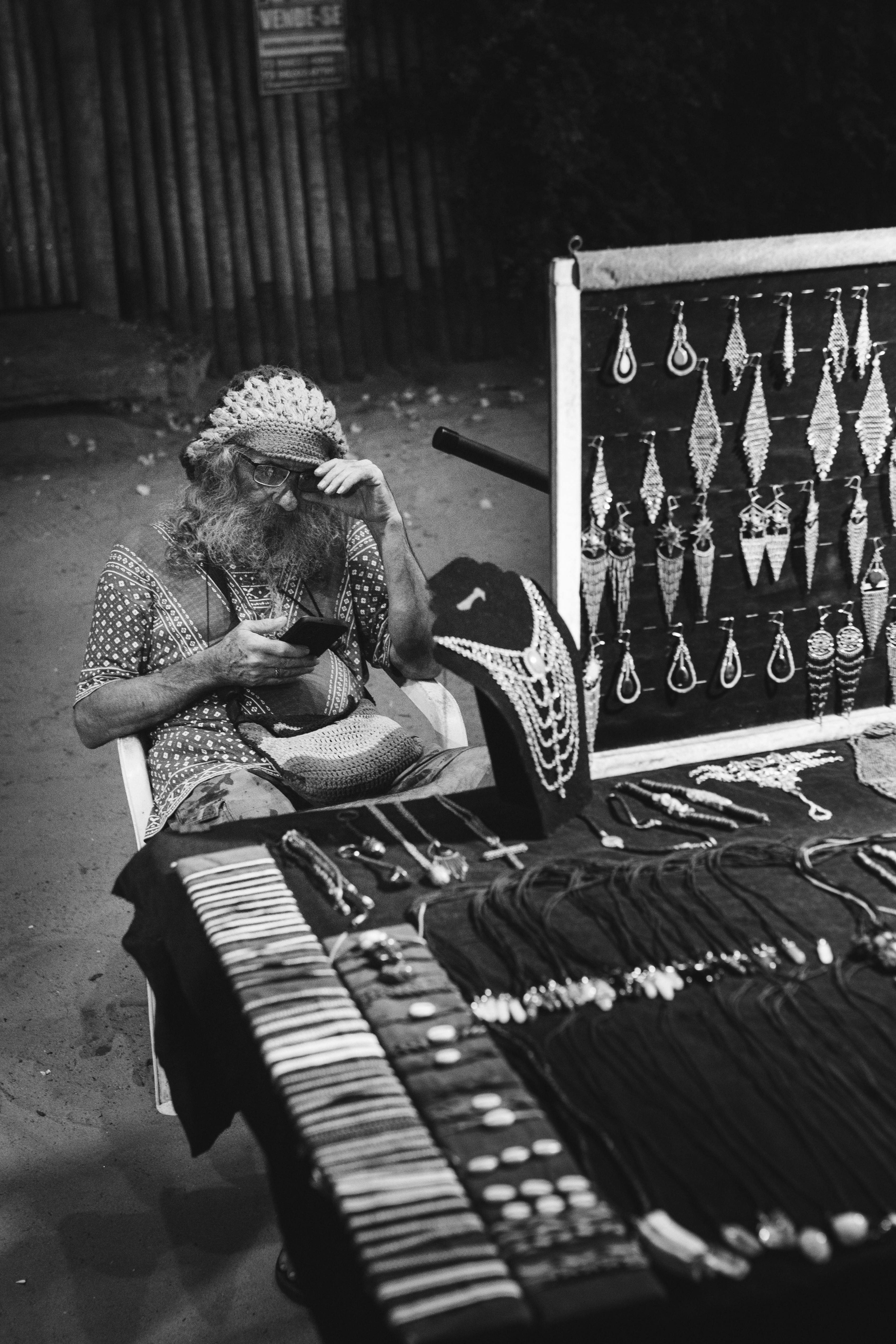 Gratis Sort-hvidt billede af en gadesælger, der fremviser håndlavede smykker i en svagt oplyst aften. Lagerfoto