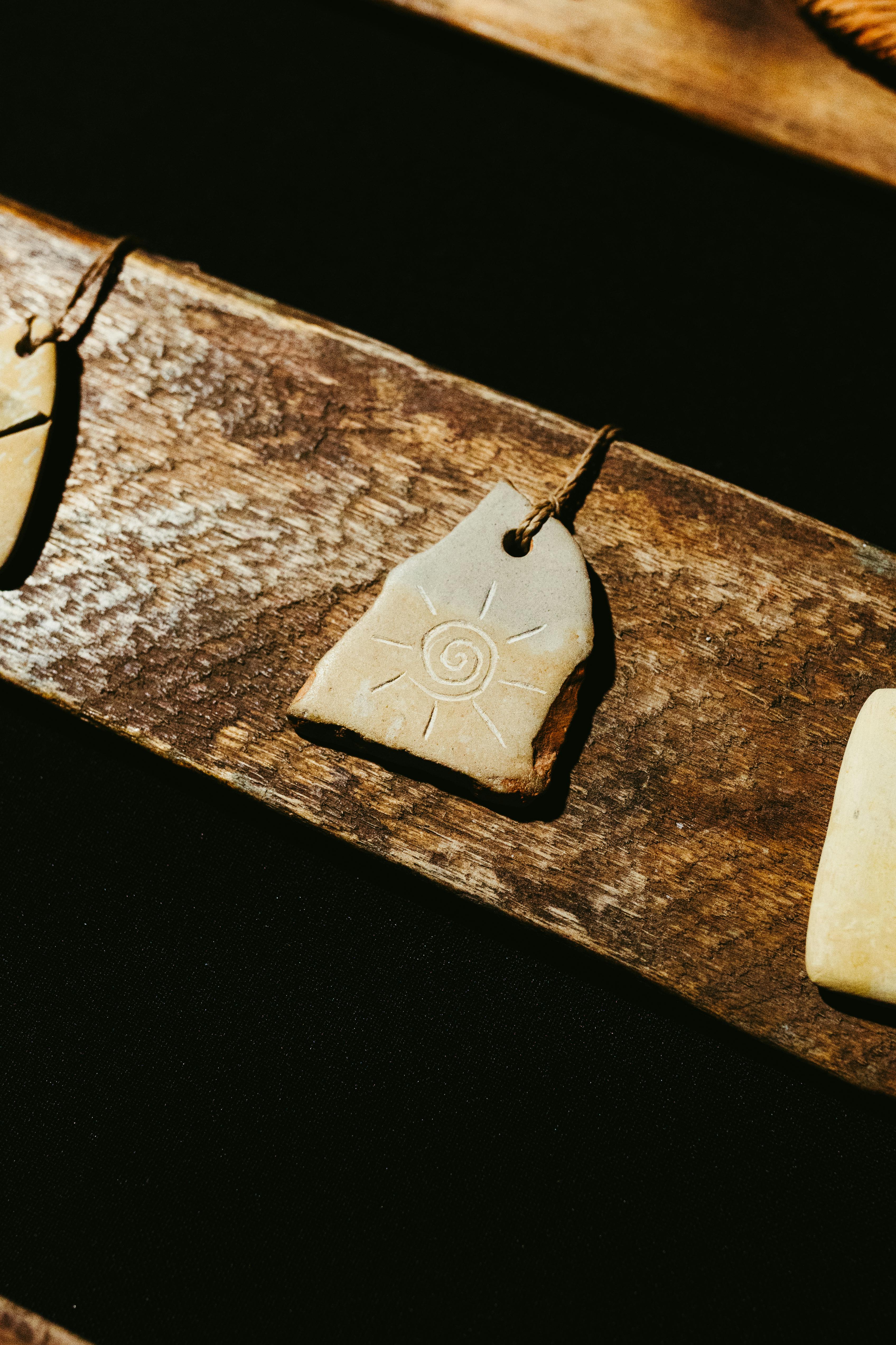 Zadarmo Detailný záber na kamenný prívesok s rytím v tvare slnečnej špirály na drevenom pozadí, ktorý evokuje pocit rustikálnej elegancie. Fotka z fotobanky