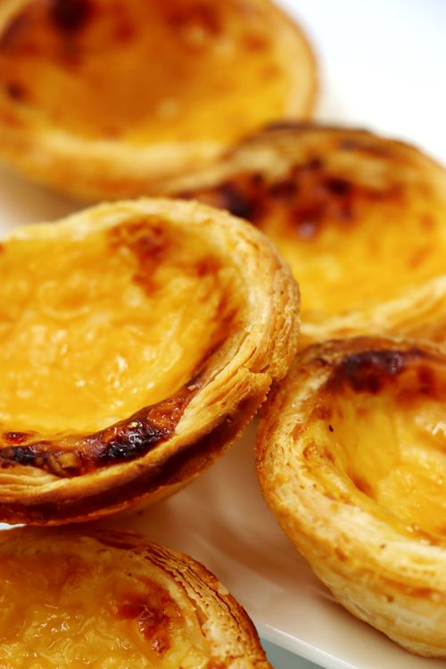 Free Close-up of traditional Portuguese custard tarts with crispy puff pastry, served on a white plate. Stock Photo