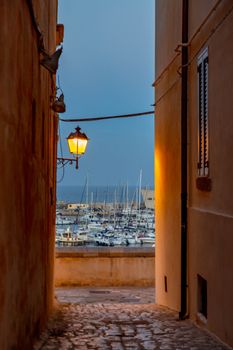 Unique view of Bari Harbor through a charming alleyway, illuminated at twilight.