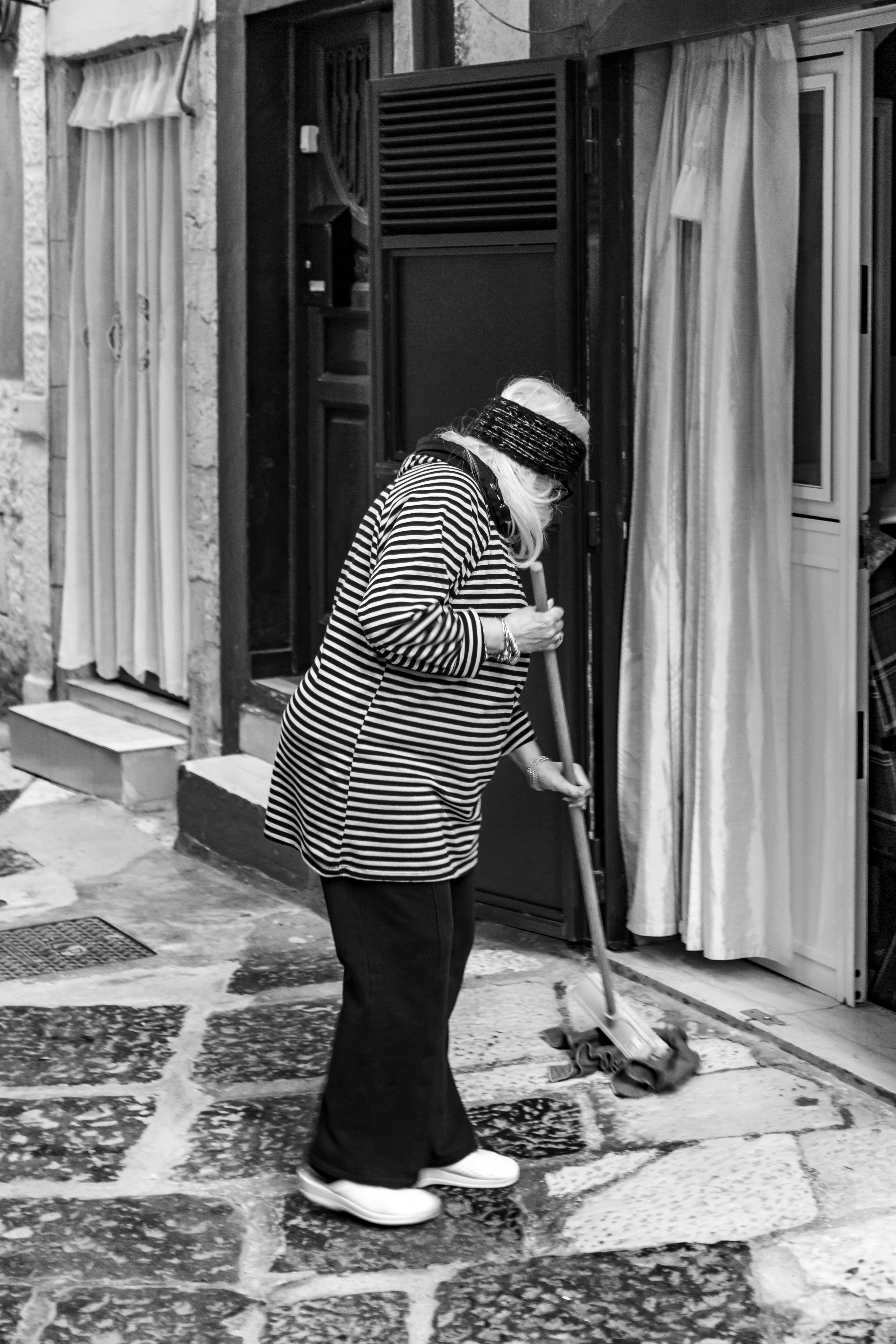 ฟรี หญิงชราคนหนึ่งกำลังกวาดถนนในเมืองบารี สะท้อนให้เห็นถึงวิถีชีวิตและวัฒนธรรมของชาวอิตาลี คลังภาพถ่าย