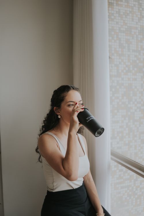 Free A woman enjoys a hot beverage by the window, embracing a moment of relaxation. Stock Photo