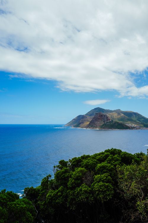 Free Vibrant coastal scene featuring lush greenery, blue ocean, and distant mountains. Stock Photo