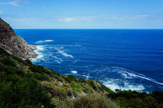 Breathtaking view of rocky cliffs and deep blue ocean waves under a clear sky.