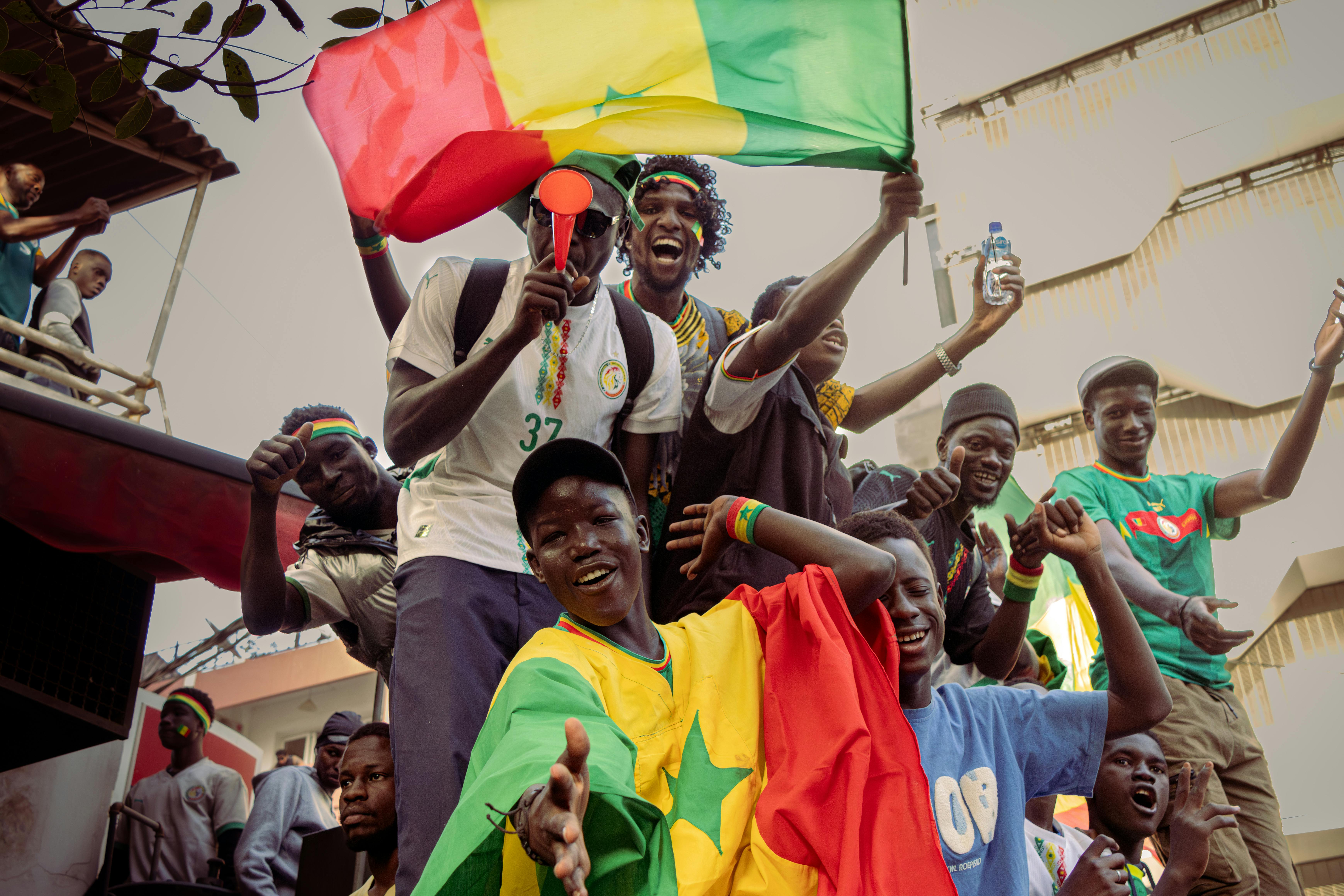 Gratuit Un groupe de personnes enthousiastes célèbrent l'événement en brandissant des drapeaux sénégalais aux couleurs chatoyantes. Scène joyeuse et colorée. Photos
