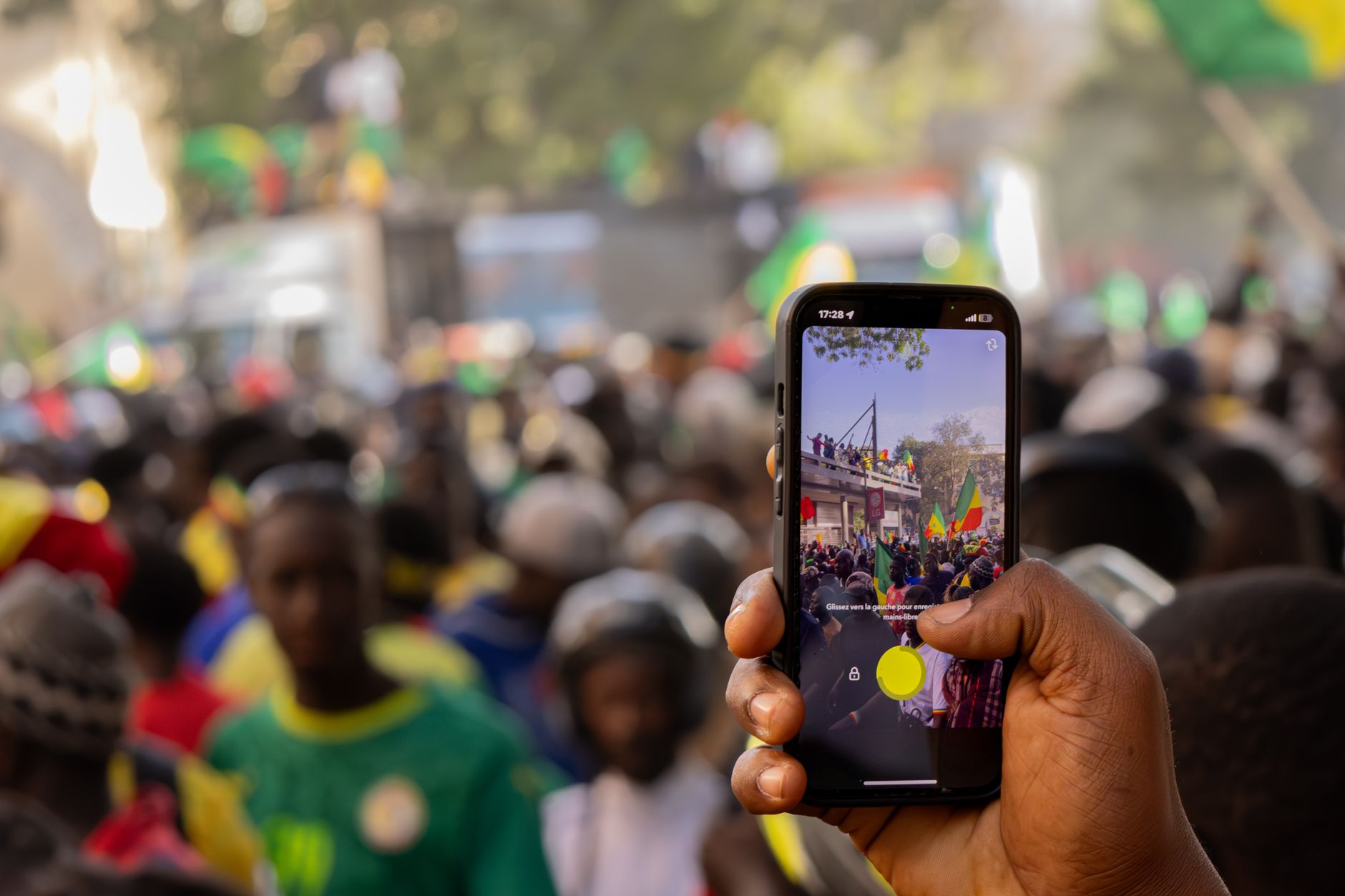 A lively street scene in Senegal with people celebrating, viewed through a smartphone screen.
