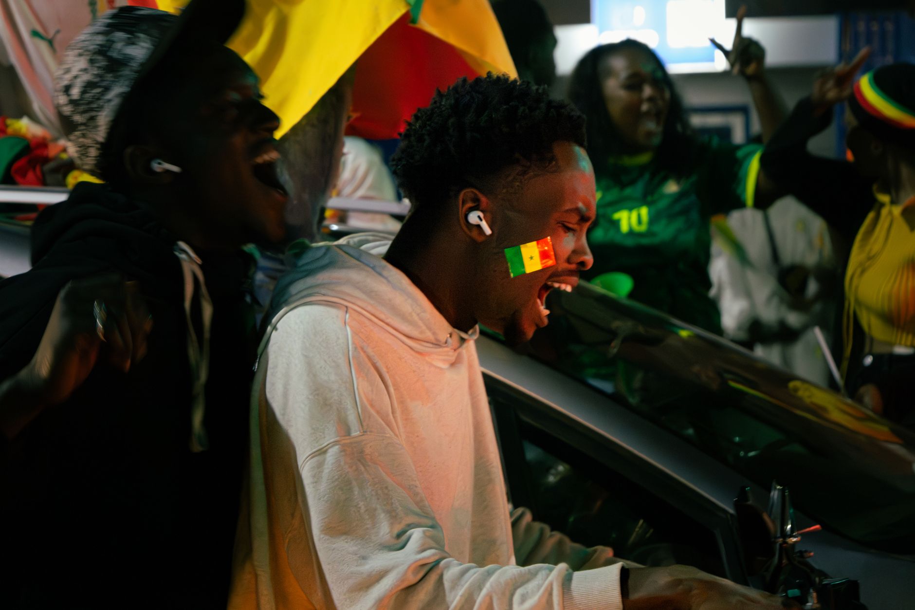 A group celebrating exuberantly with the Senegalese flag painted on a man's face, capturing vibrant street energy.