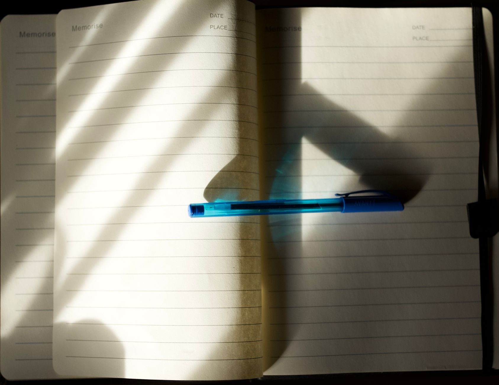 An open notebook with a blue pen in natural sunlight, casting shadows.
