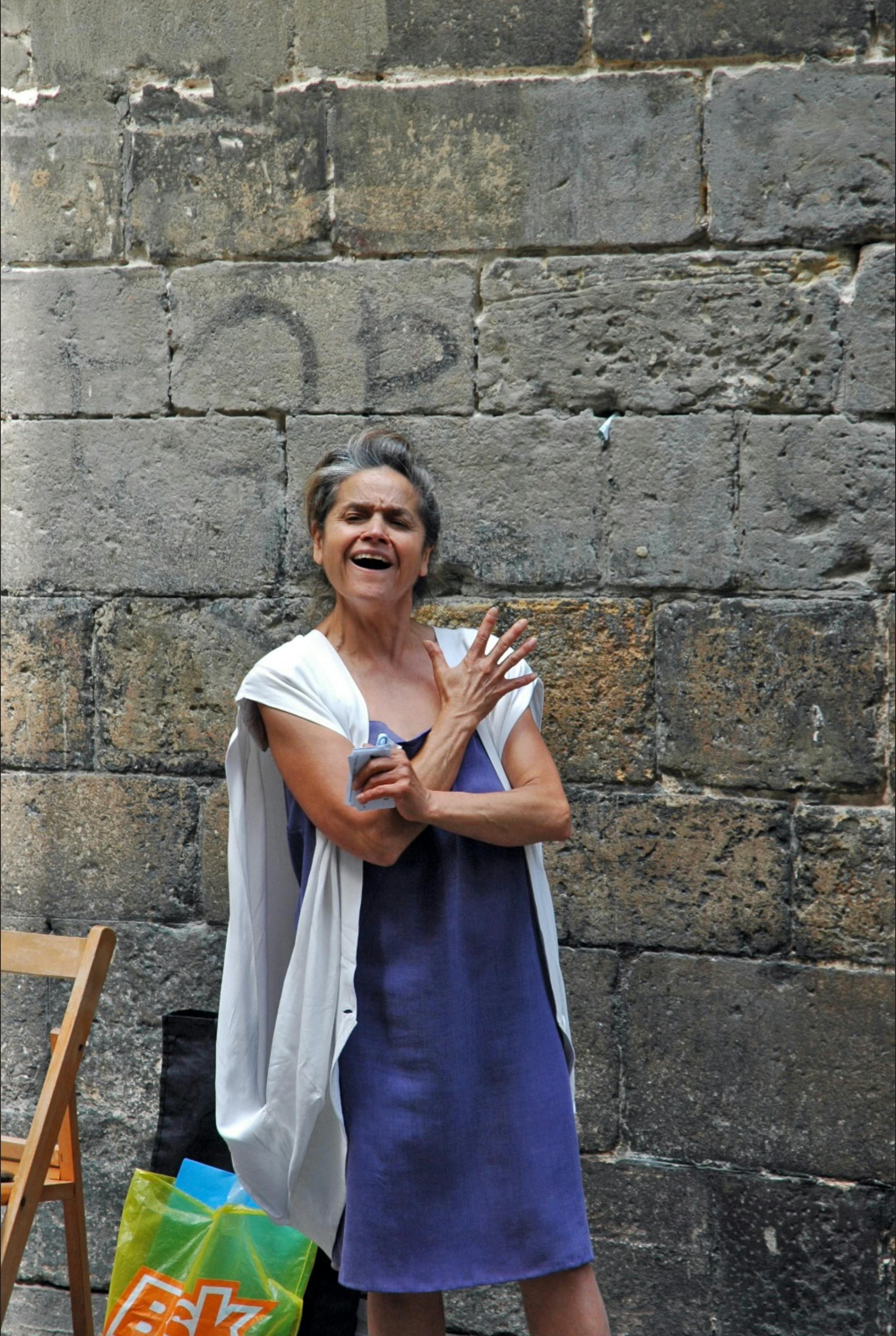 Zadarmo Usmievavá žena v modrých šatách spievajúca pri kamennom múre. Živé vonkajšie prostredie. Fotka z fotobanky