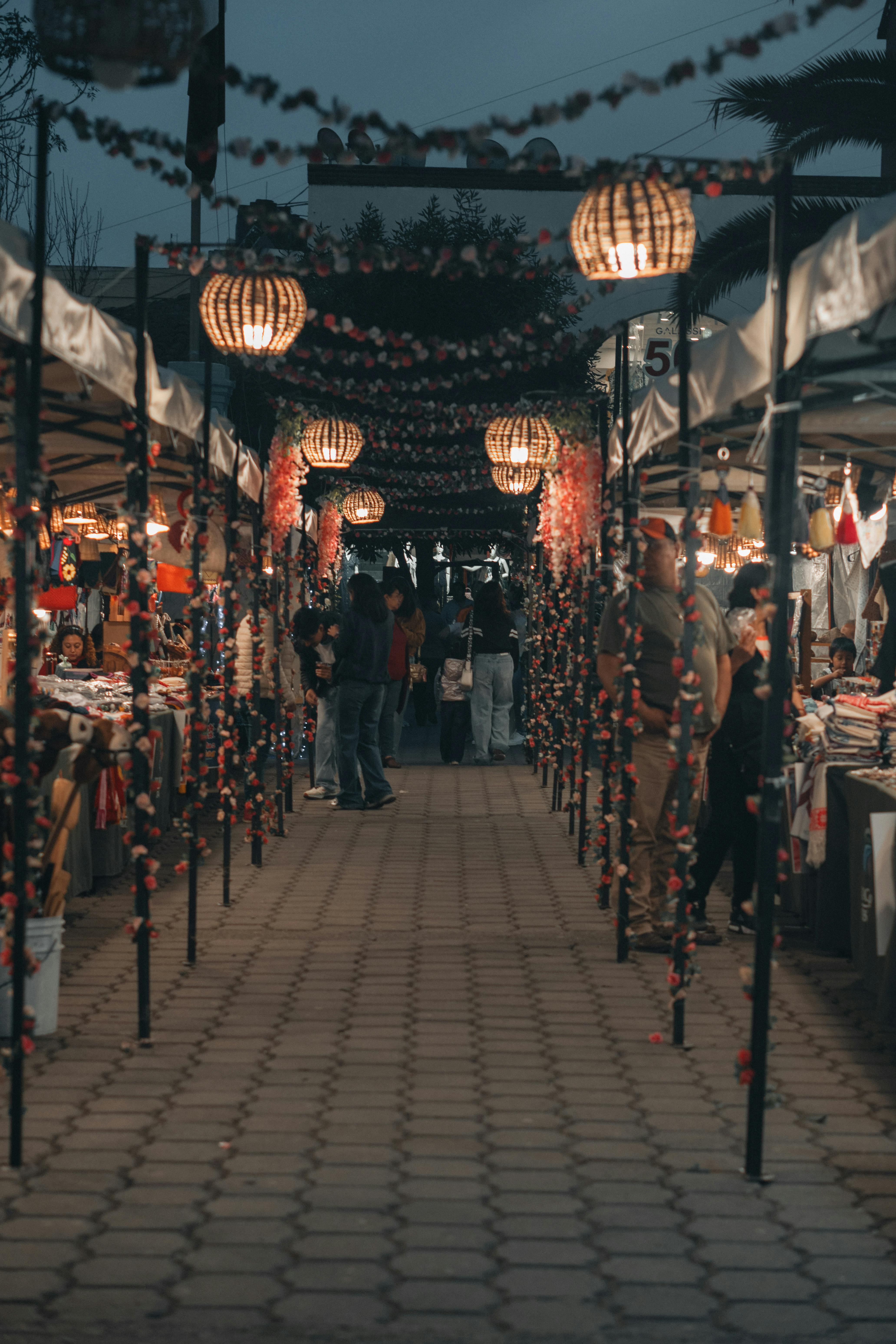 ฟรี ภาพถ่ายบรรยากาศยามเย็นของตลาดกลางแจ้งที่คึกคักไปด้วยโคมไฟแขวนและผู้คนพลุกพล่าน คลังภาพถ่าย