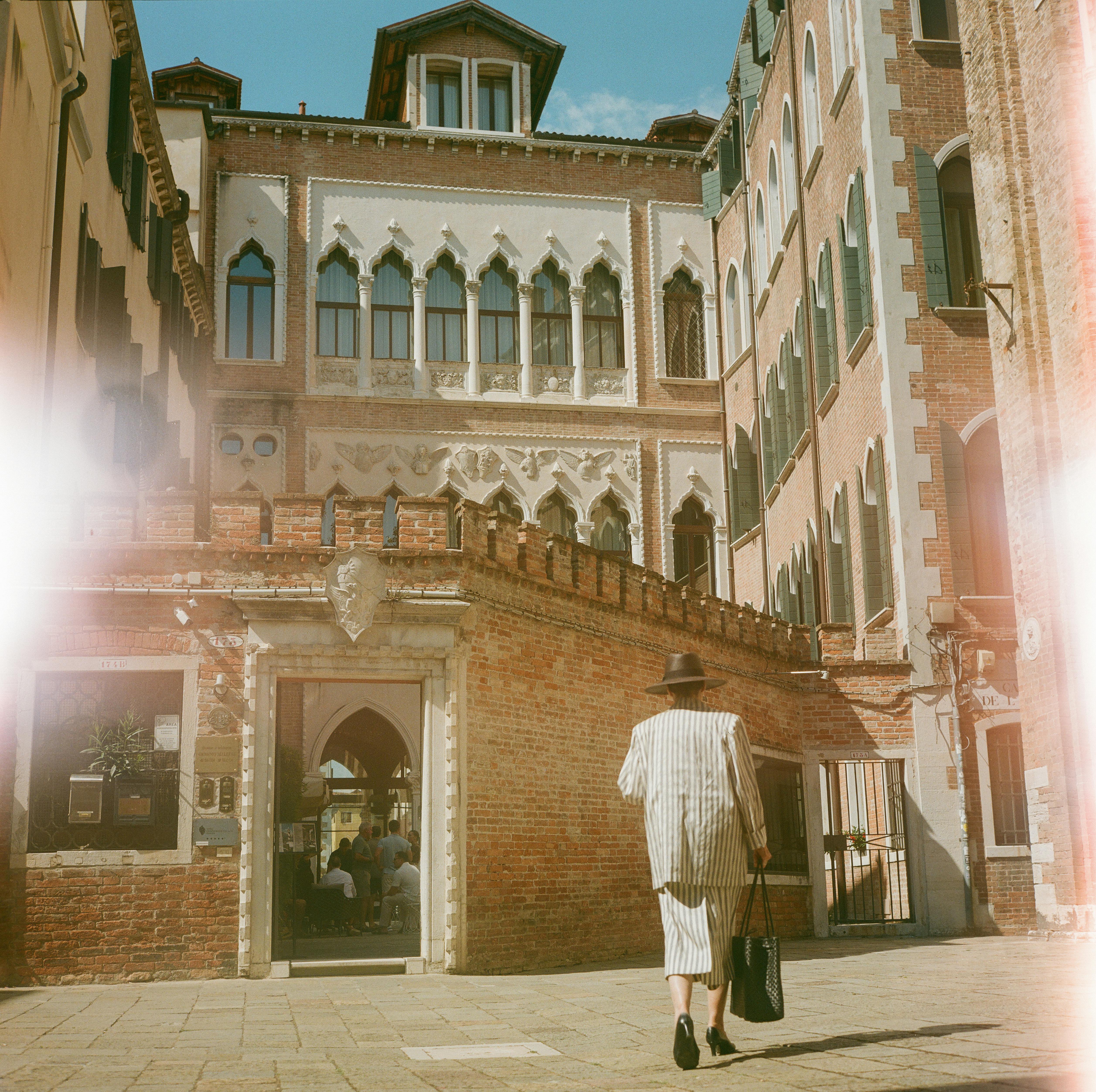 Miễn phí Một người phụ nữ sành điệu trong bộ trang phục kẻ sọc đi ngang qua một tòa nhà lịch sử ở Venice, Ý, ghi lại trọn vẹn tinh túy của kiến ​​trúc và thời trang Venice. Ảnh lưu trữ