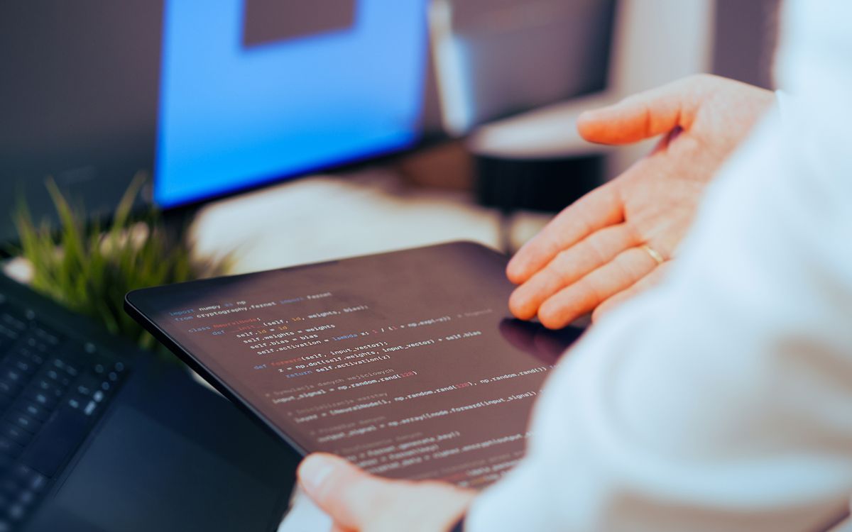 Software developer analyzing code on a tablet in a modern office workspace.