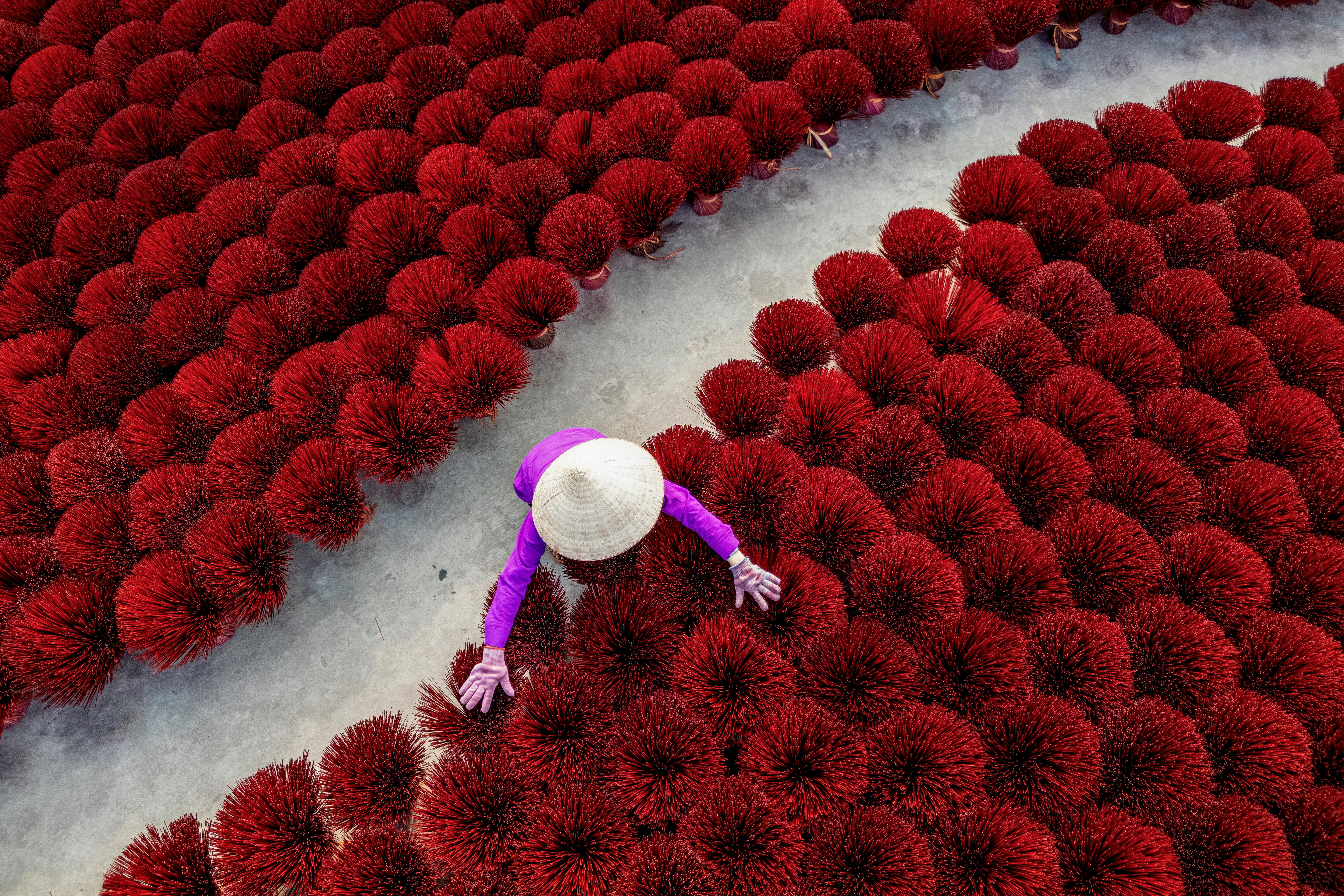 Безкоштовне Знімок зверху, на якому видно працівника, який упорядковує червоні ароматичні палички, розкладені для сушіння, демонструючи яскраві кольори та традиційну майстерність. стокове фото