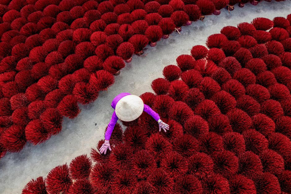 An overhead shot of a worker organizing red incense sticks laid out to dry, showcasing vibrant colors and traditional craftsmanship.