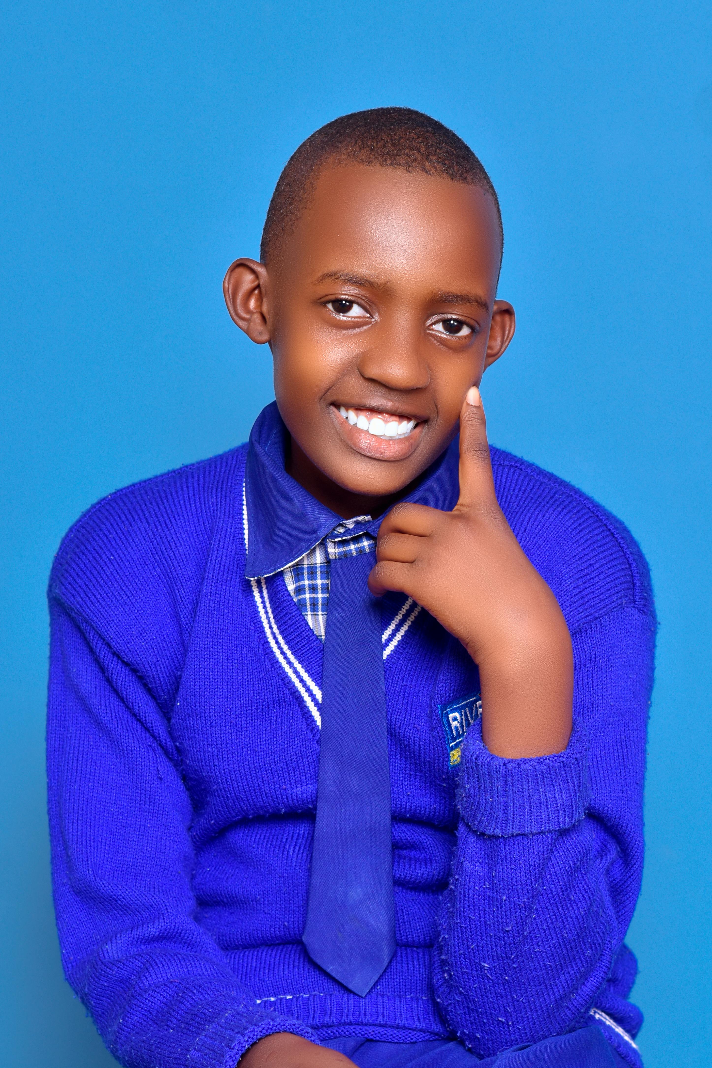 Young boy smiling in a blue school uniform against a blue background.