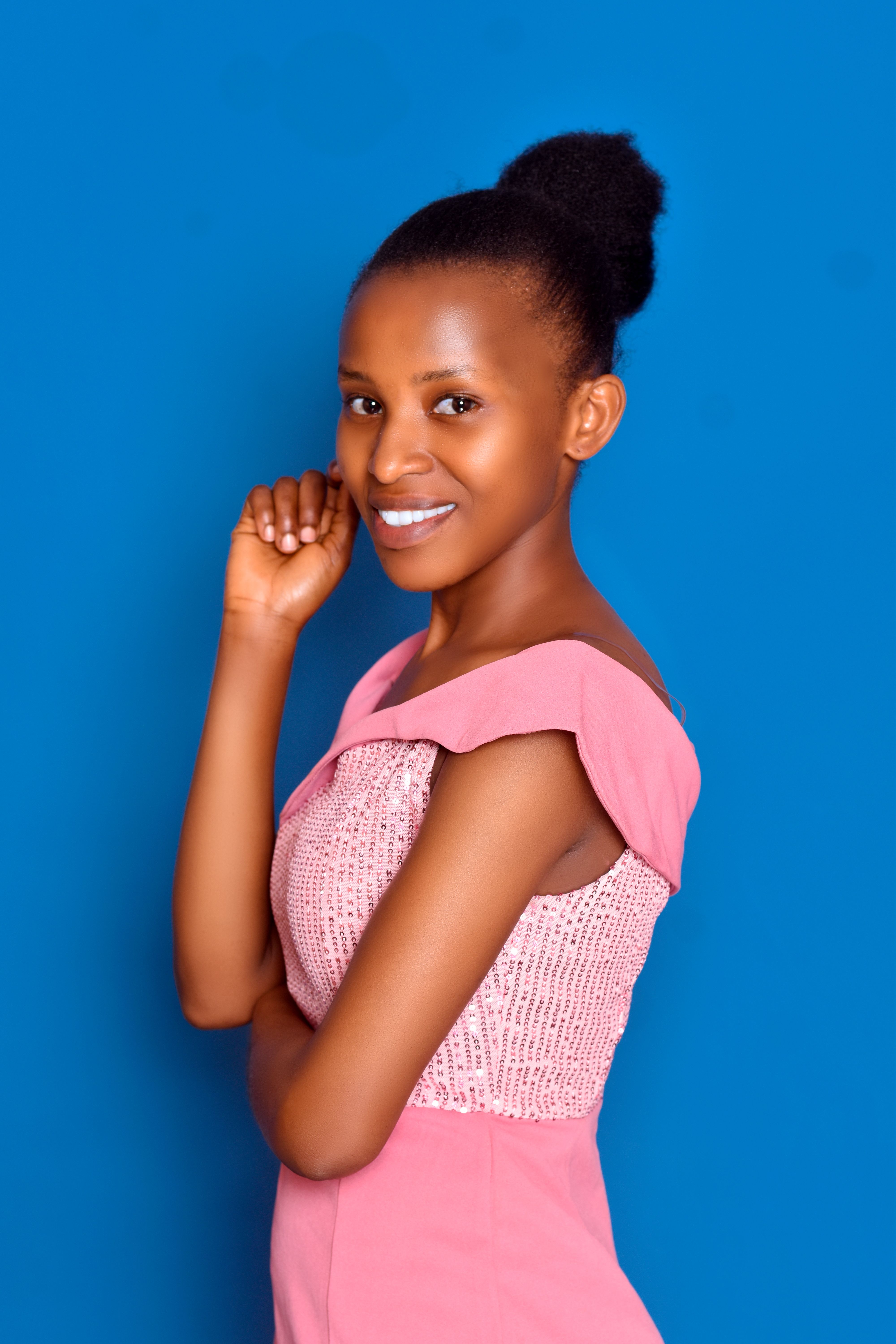 Beautiful woman in a pink dress posing with a cheerful smile on a blue background.