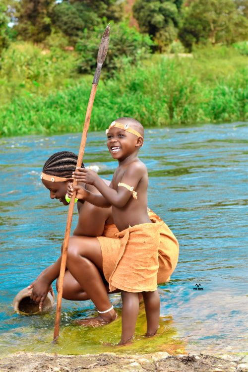 Free Children joyfully playing by a river, wearing traditional clothing and holding a spear. Stock Photo