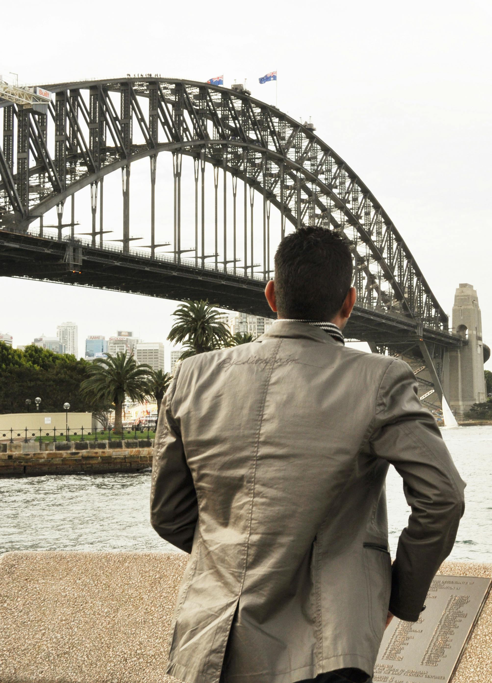 Безкоштовне Чоловік у повсякденному костюмі милується культовим мостом Харбор-Брідж у Сіднеї з набережної. стокове фото