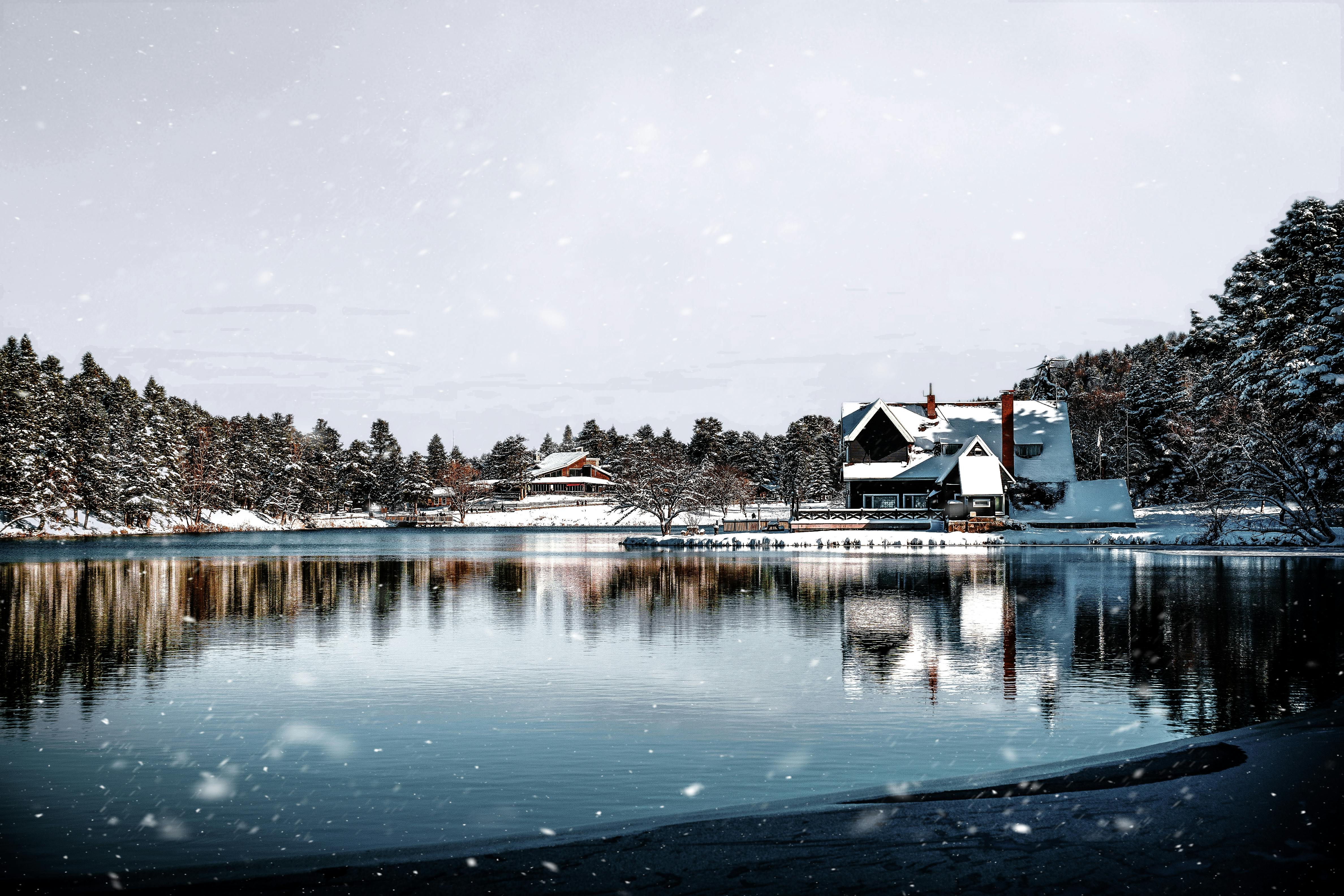 ingyenes Egy békés téli jelenet egy hófödte faházzal egy fákkal körülvett, nyugodt tó partján. Stockfotó