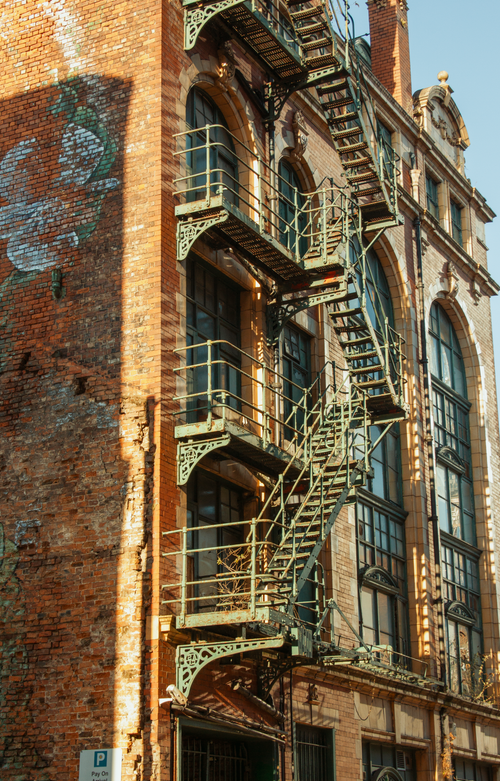 Free A historic industrial building in Manchester featuring a distinctive metal staircase against a brick facade. Stock Photo