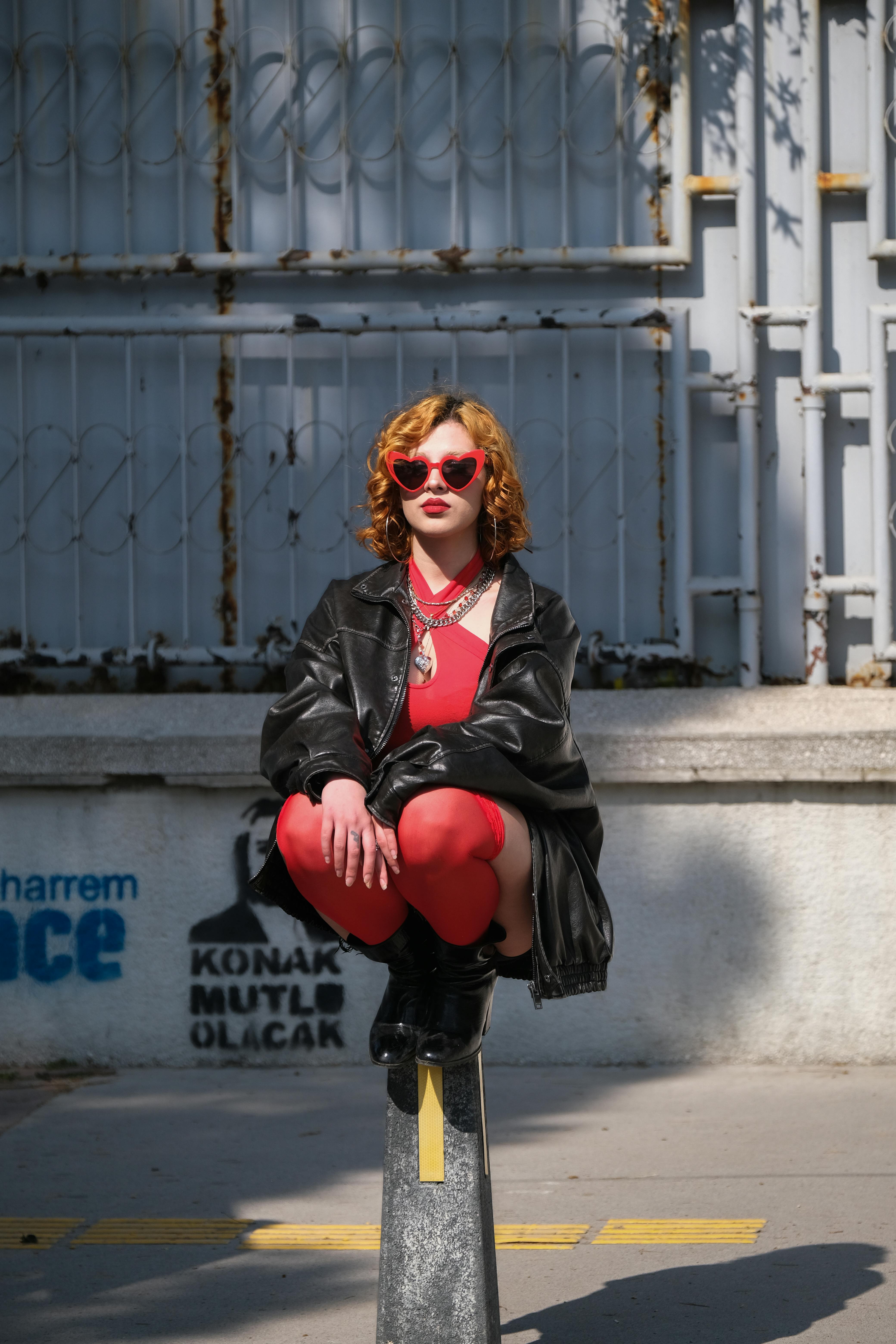 무료 붉은색 의상과 하트 모양 선글라스를 착용한 세련된 여성이 도시 풍경 속에서 포즈를 취하며 도시적인 시크함을 발산하고 있다. 스톡 사진