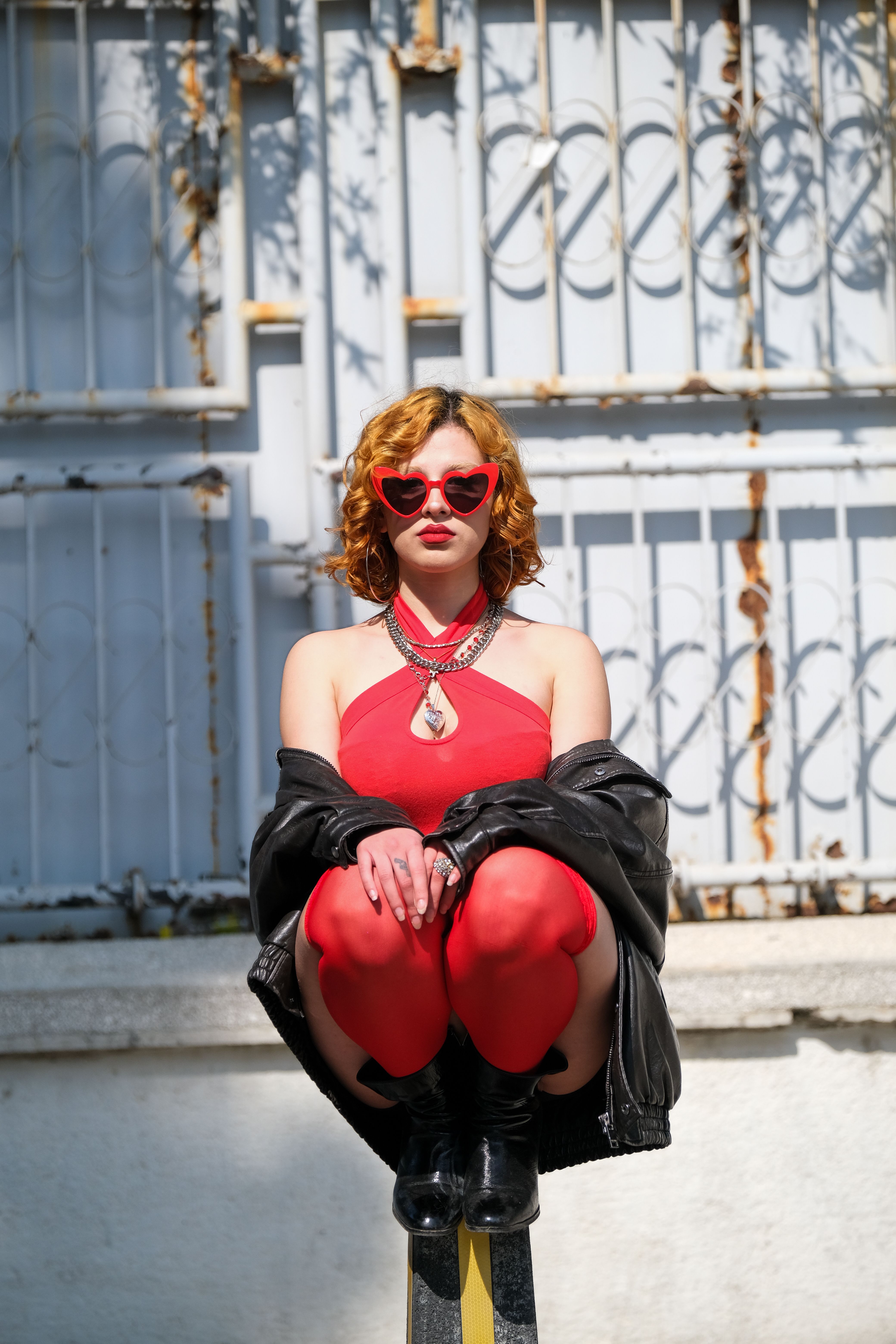 Stylish woman in red dress with heart-shaped sunglasses sitting outdoors.
