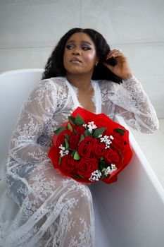 Woman in lace outfit holding red roses in a bathtub setting.