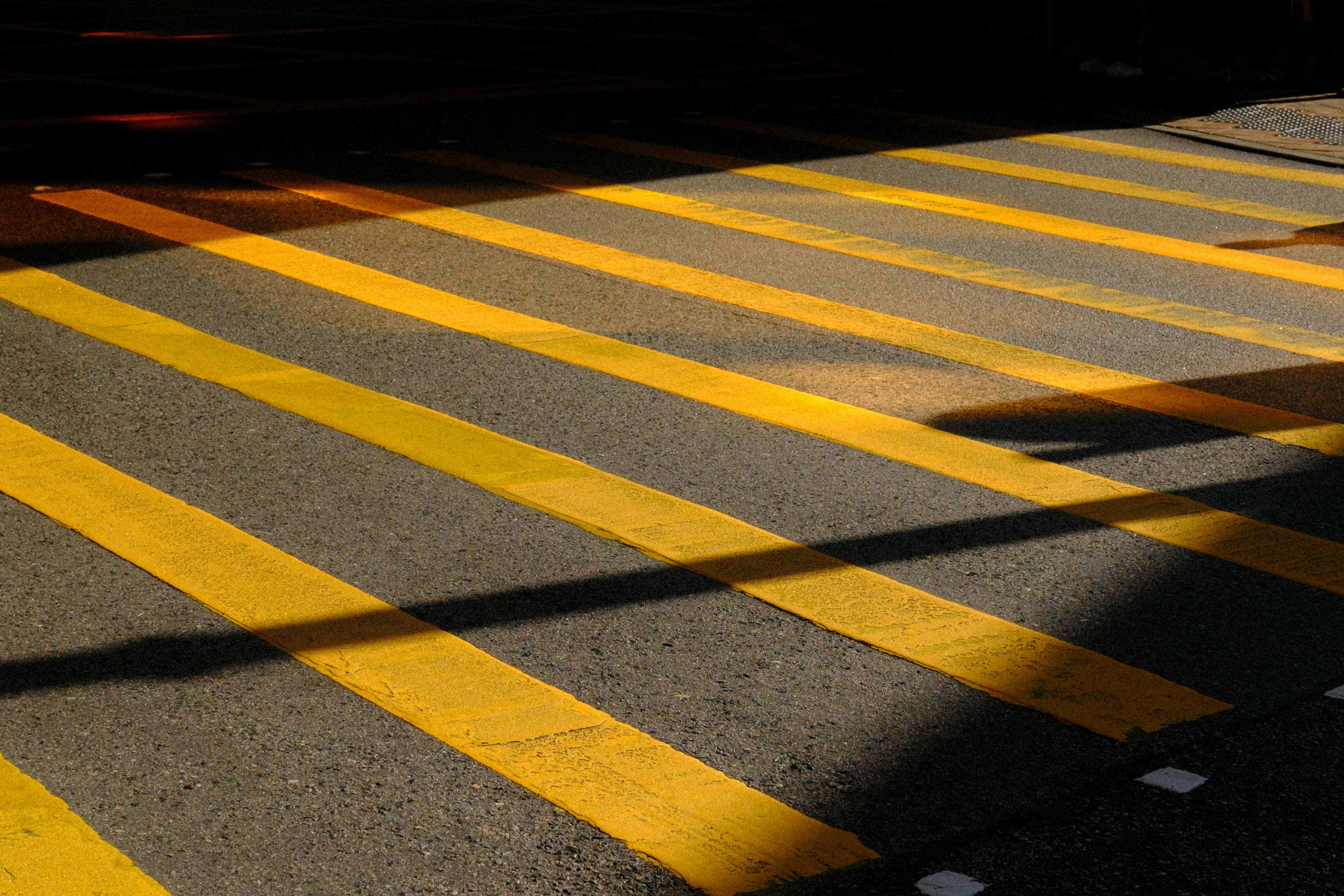 Zadarmo Dynamický pohľad na žlto pruhovaný priechod pre chodcov v kontrastnom svetle a tieňoch. Fotka z fotobanky
