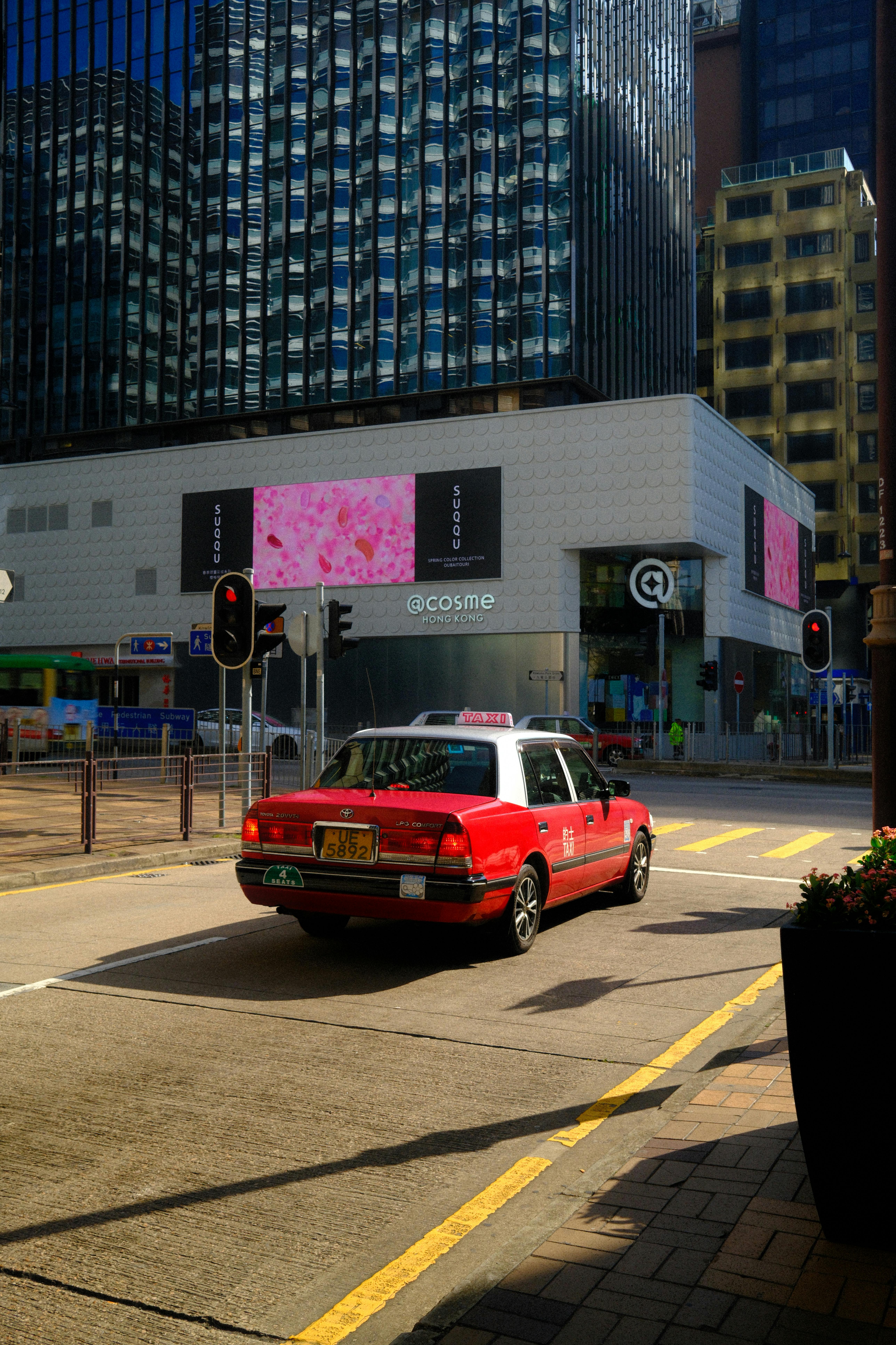 Безкоштовне Класичне червоне таксі їде жвавими вулицями Гонконгу, обрамленими сучасними хмарочосами. стокове фото