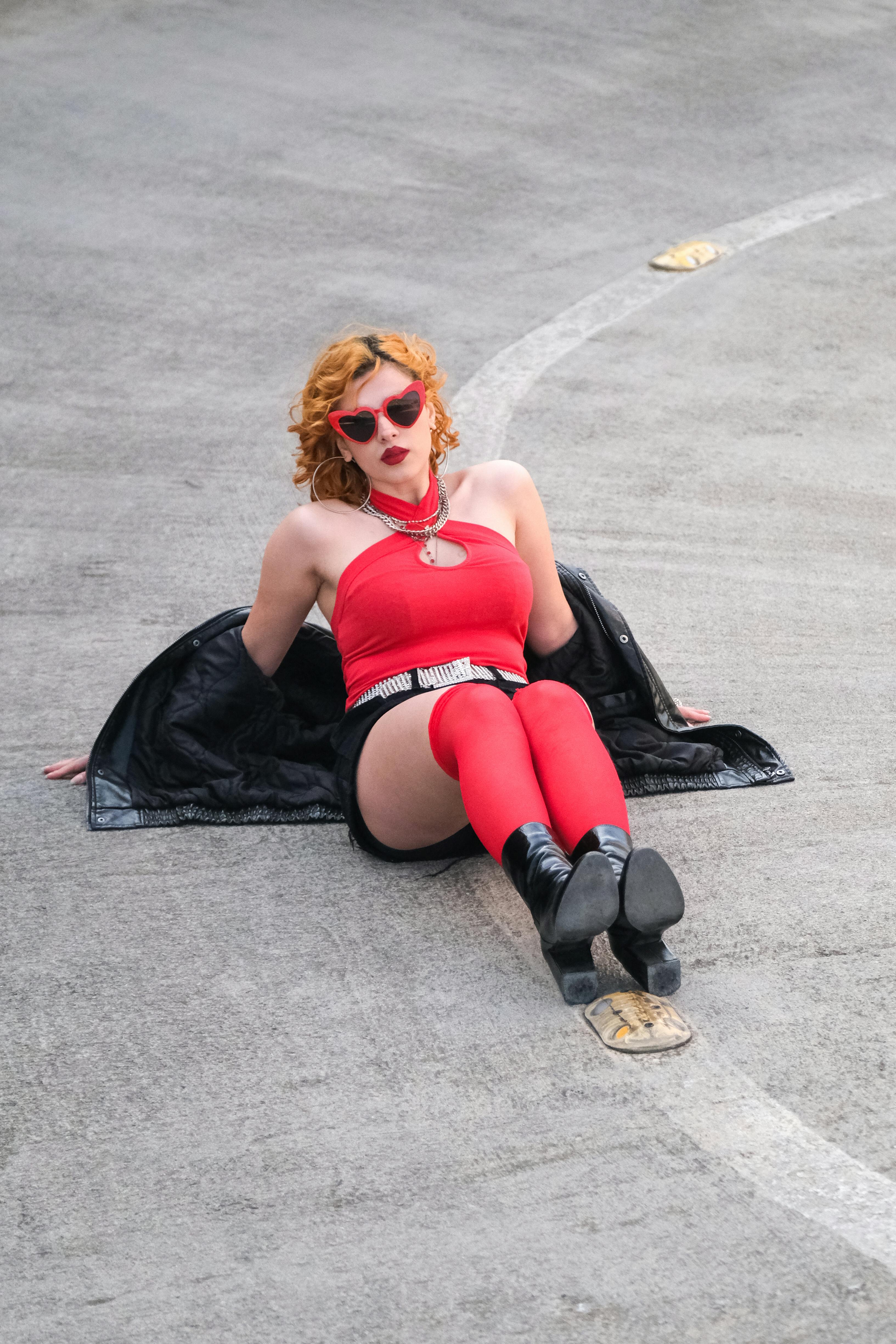 ฟรี หญิงสาวทันสมัยในชุดสีแดงกำลังพักผ่อนอยู่บนทางเท้าในเมือง เปล่งประกายด้วยความมั่นใจและมีสไตล์ คลังภาพถ่าย