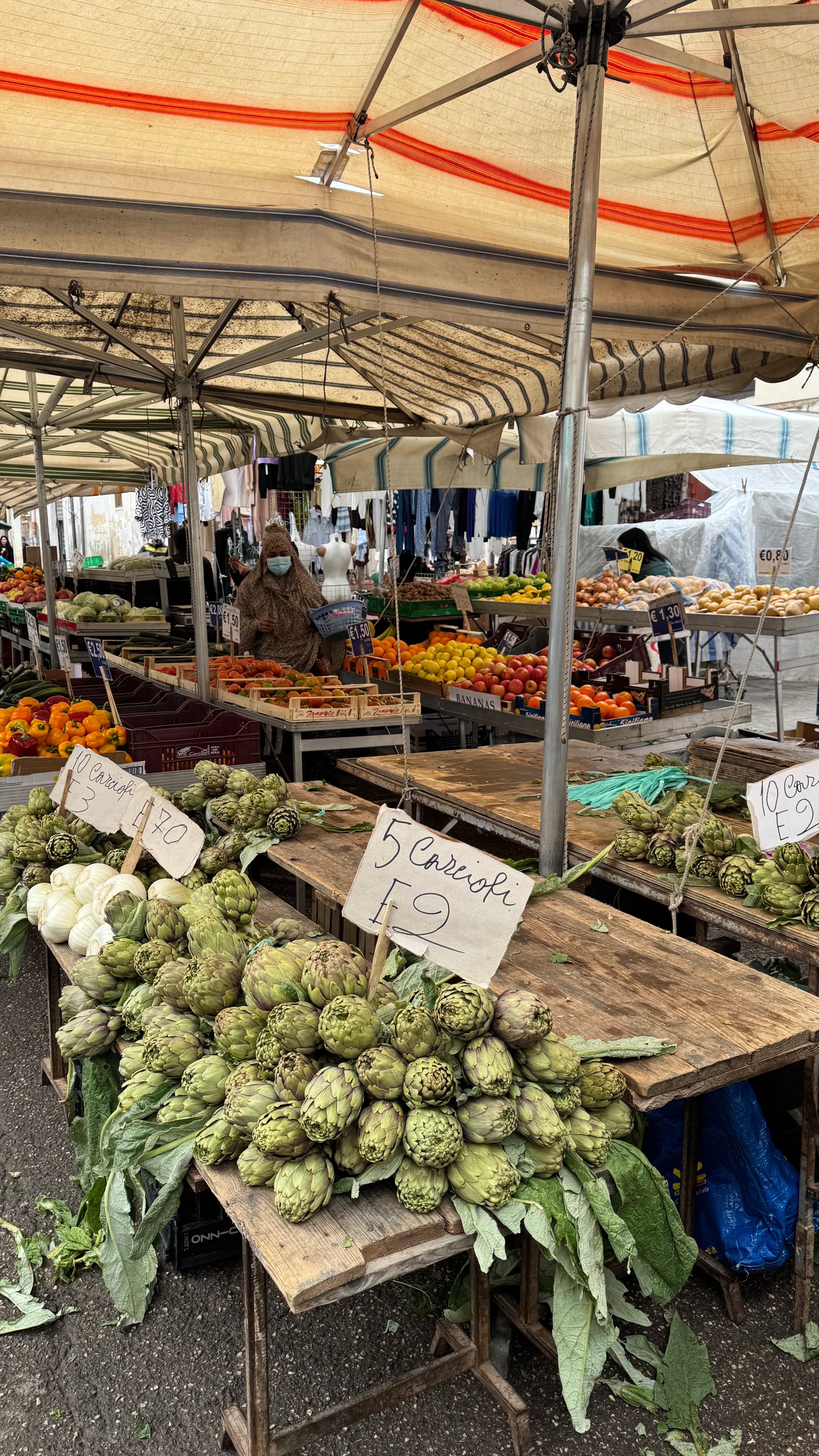 Fotomural Un mercado al aire libre en Italia que exhibe una gran variedad de alcachofas frescas y productos agrícolas coloridos a la venta.