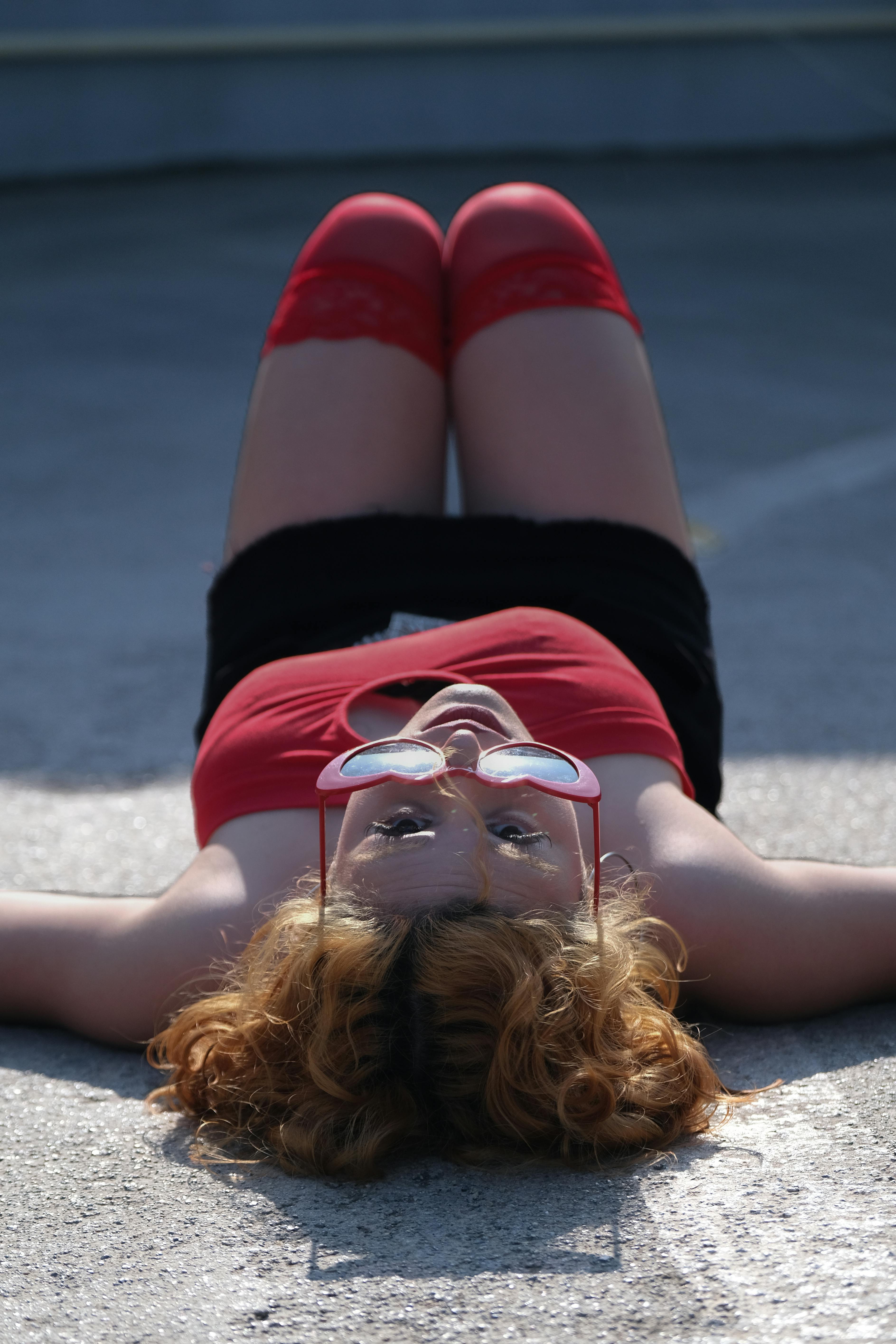 ingyenes Egy piros nyári ruhás nő fekszik a járdán, élvezi a napsütéses napot. Stockfotó