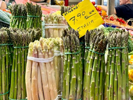 White and green asparagus bundles on display at a vibrant Italian market.