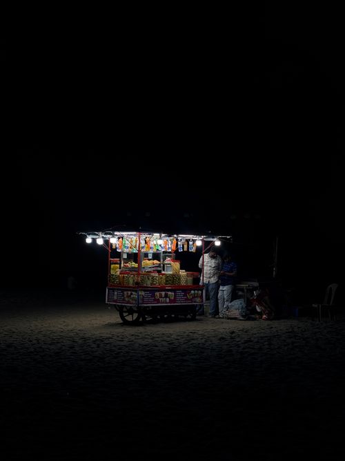 Free Illuminated street vendor cart at night on a dark sandy beach providing snacks. Stock Photo