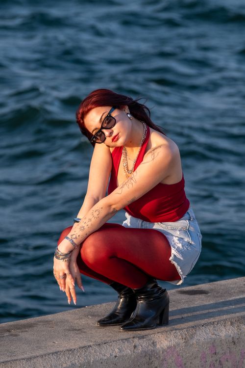 Free Fashionable woman with tattoos poses on a sunny day by the water. Stock Photo