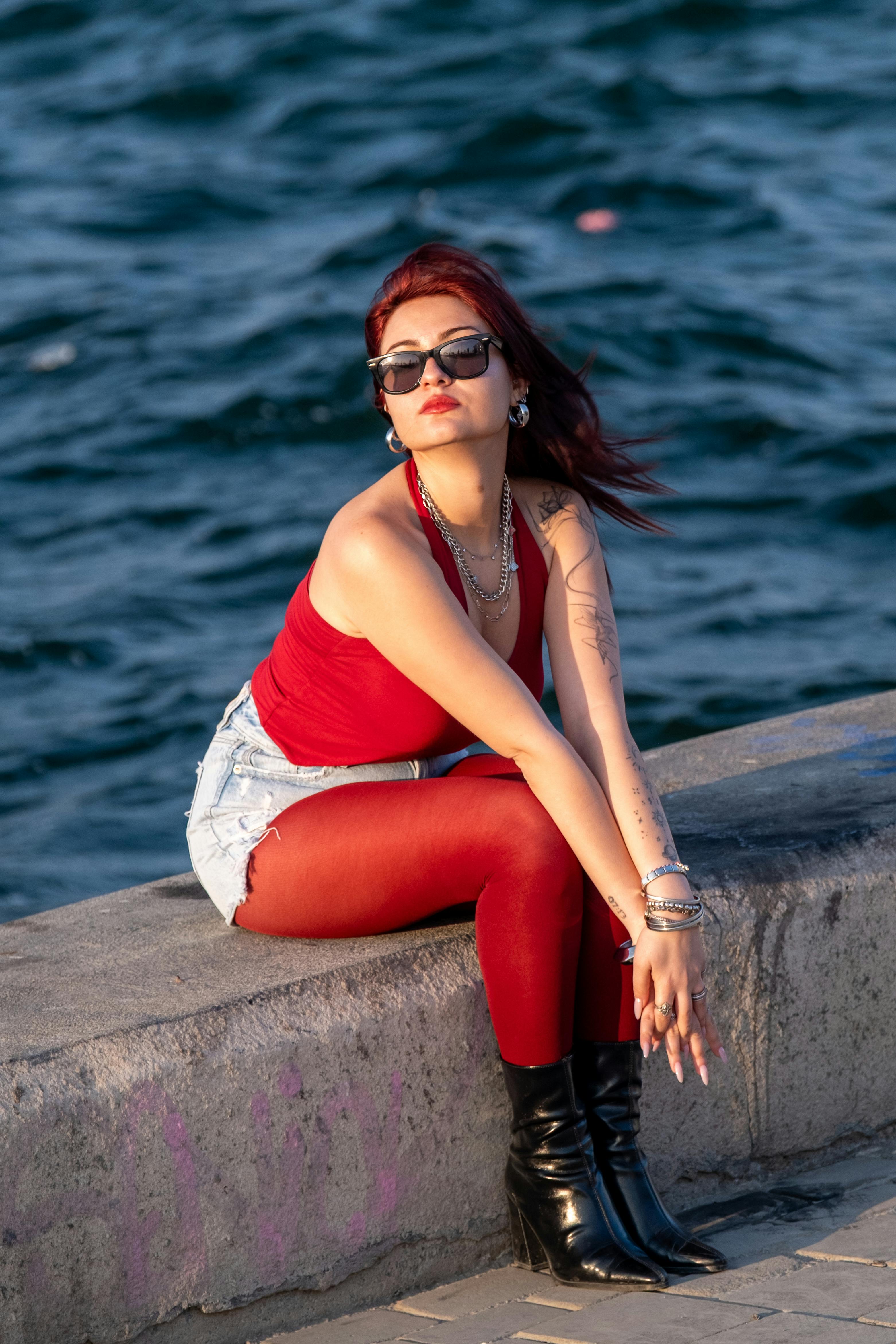 ingyenes Stílusos nő napszemüvegben ül az óceán partján, élvezve a napsütéses napot. Stockfotó