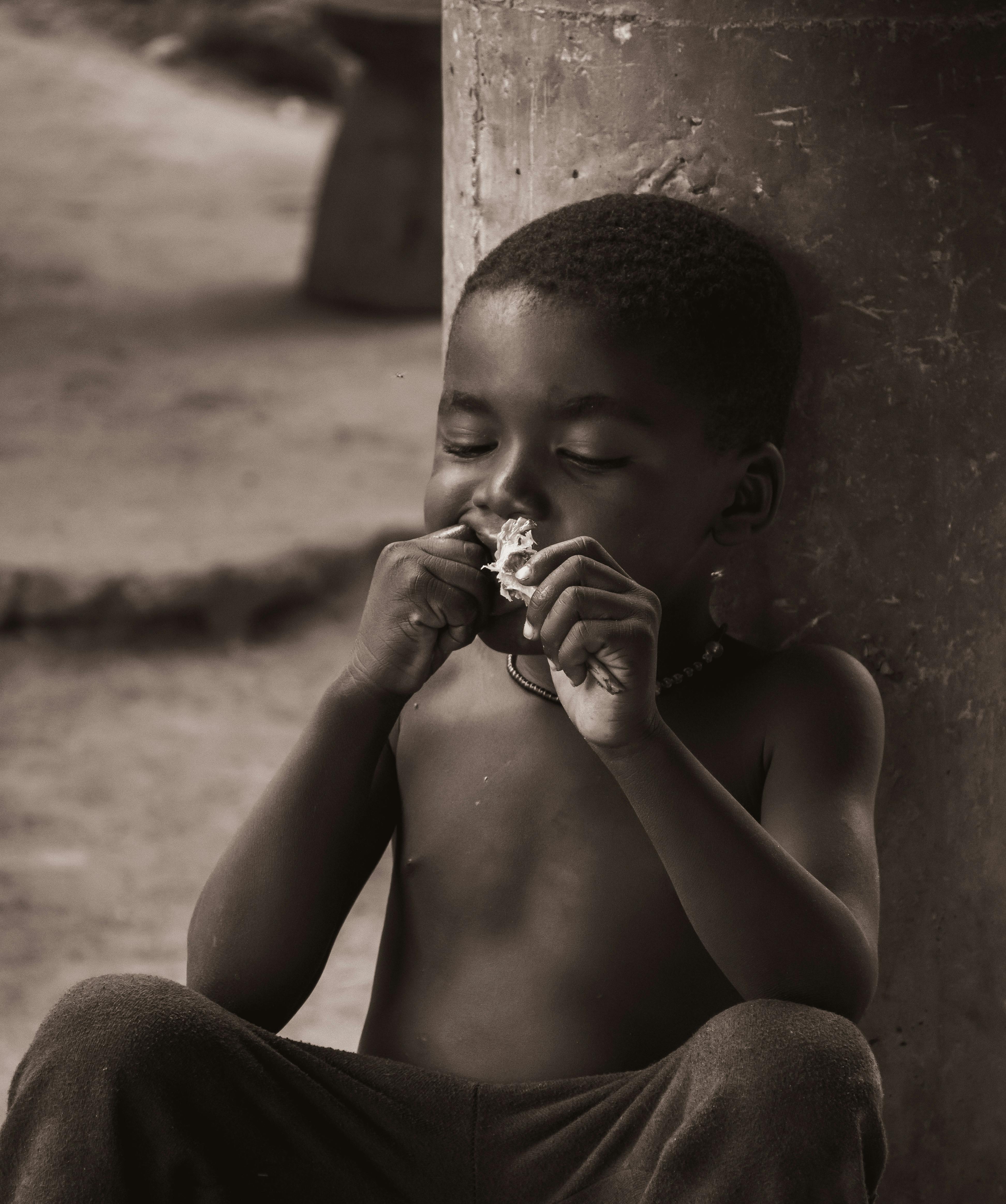 免費 一個快樂的孩子靠在戶外的柱子上，一邊吃零食一邊享受美食。 圖庫相片