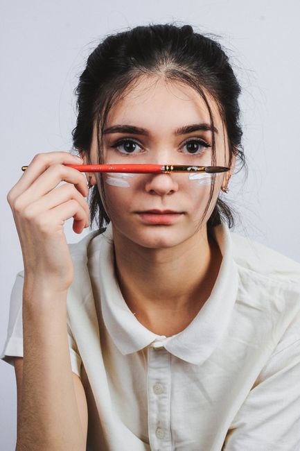 Portrait of a young woman holding a paintbrush with a serious expression indoors.