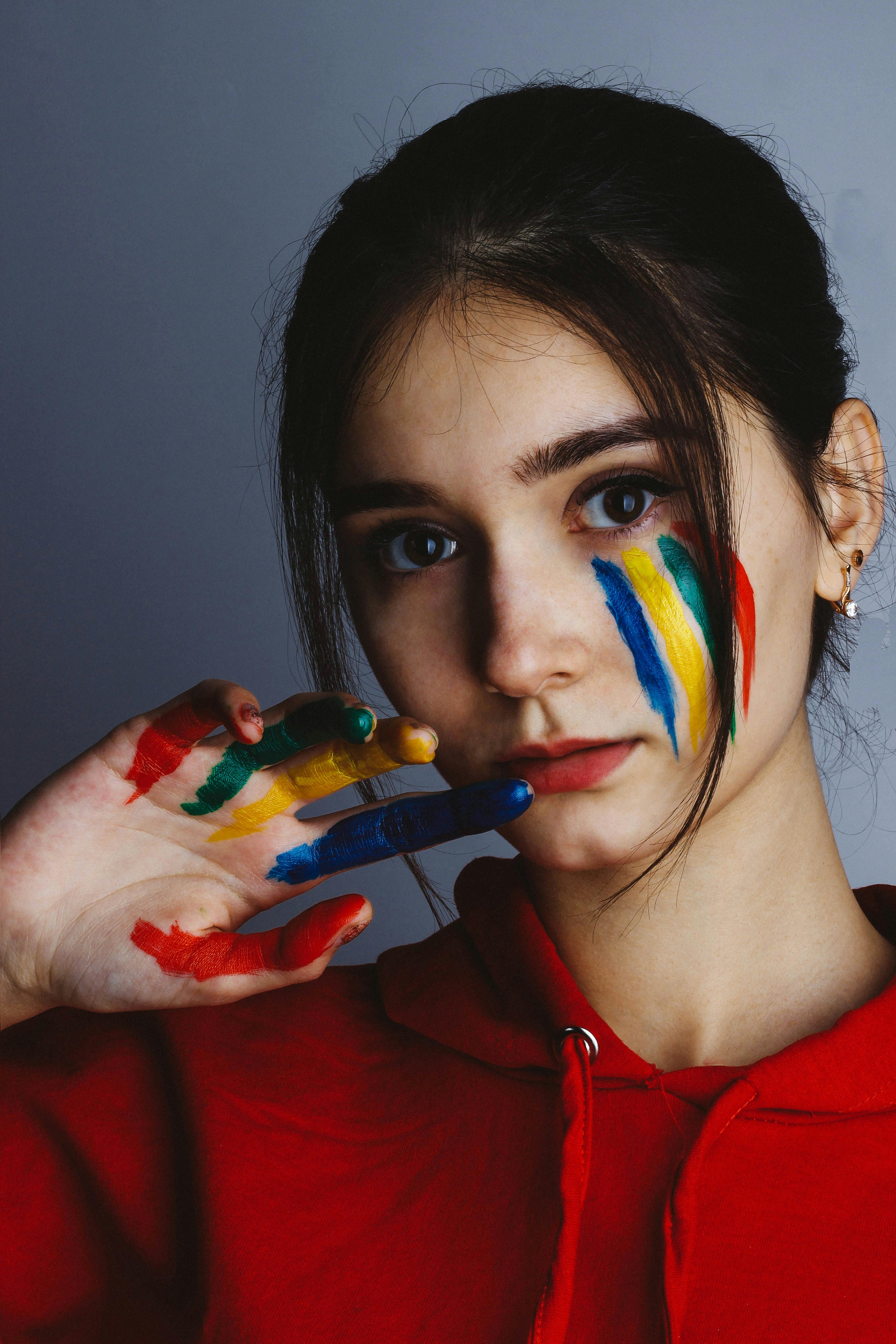 woman in red hoodie with multicolored paint on face