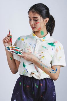 年轻的女艺术家穿着沾满油漆的衣服，手里拿着调色板和画笔