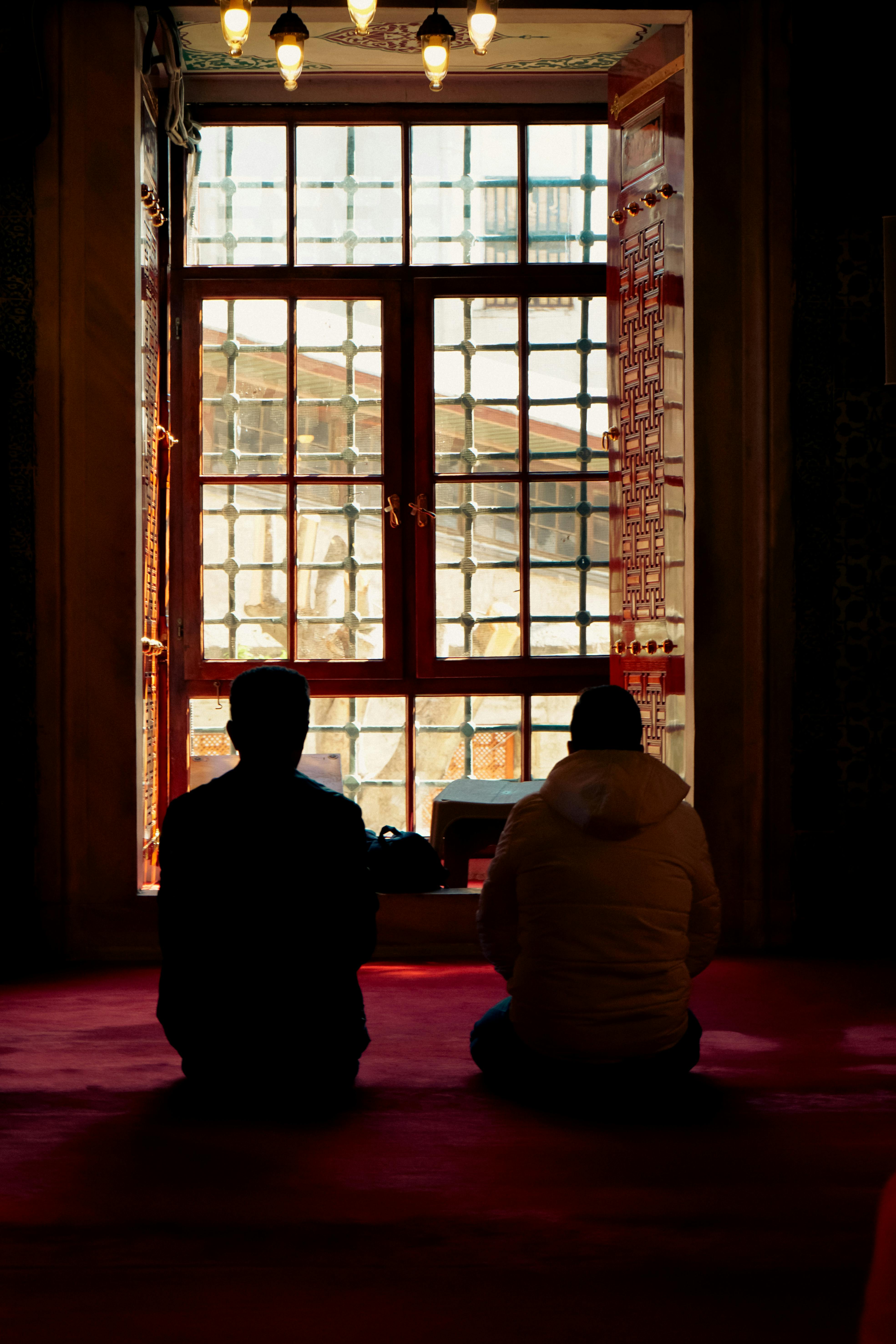 免費 兩人靜靜地坐著沉思，身影映襯在陽光照射的窗戶前。室內場景。 圖庫相片