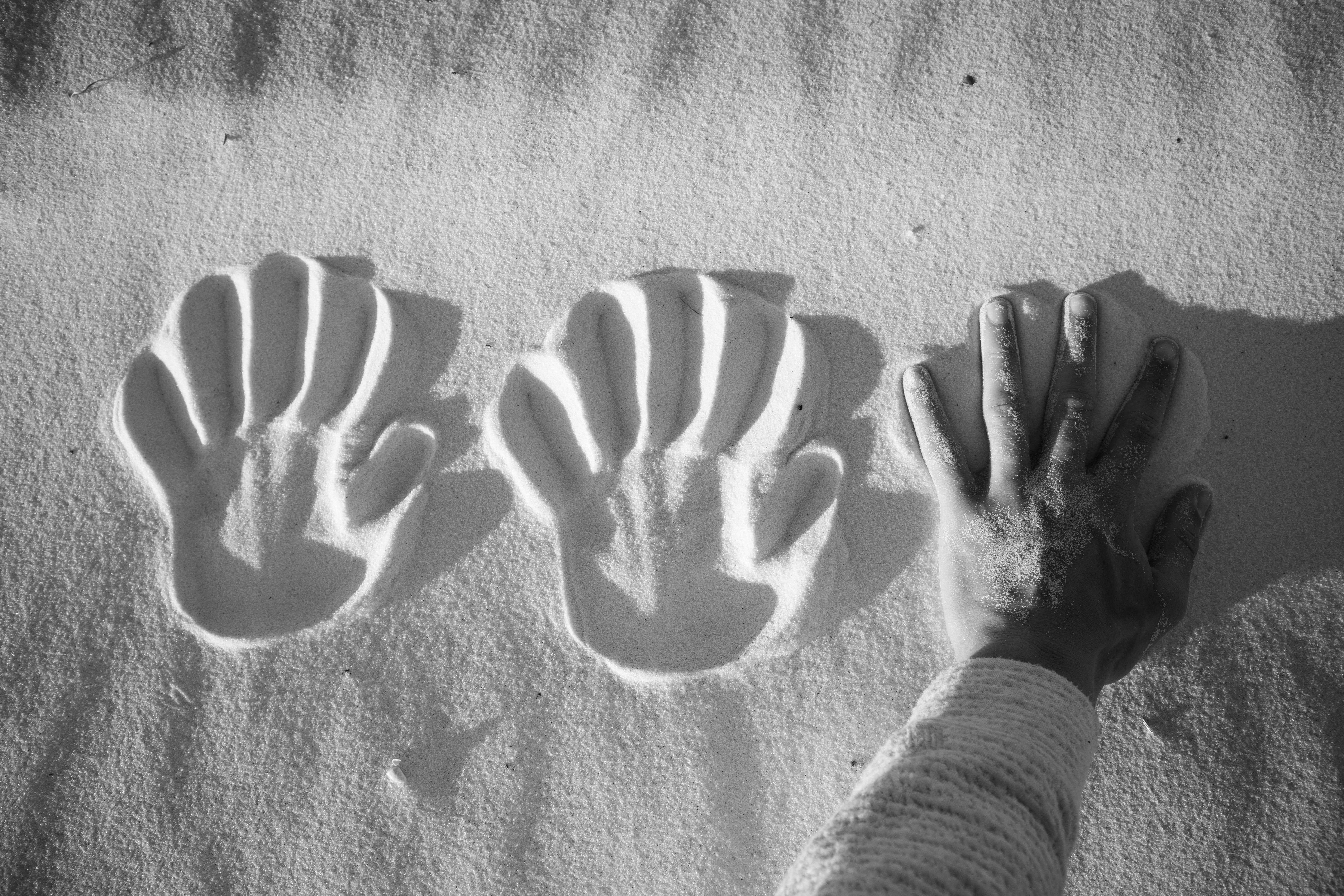 A hand pressing into the sand alongside two clear hand imprints at Santa Rosa Beach.