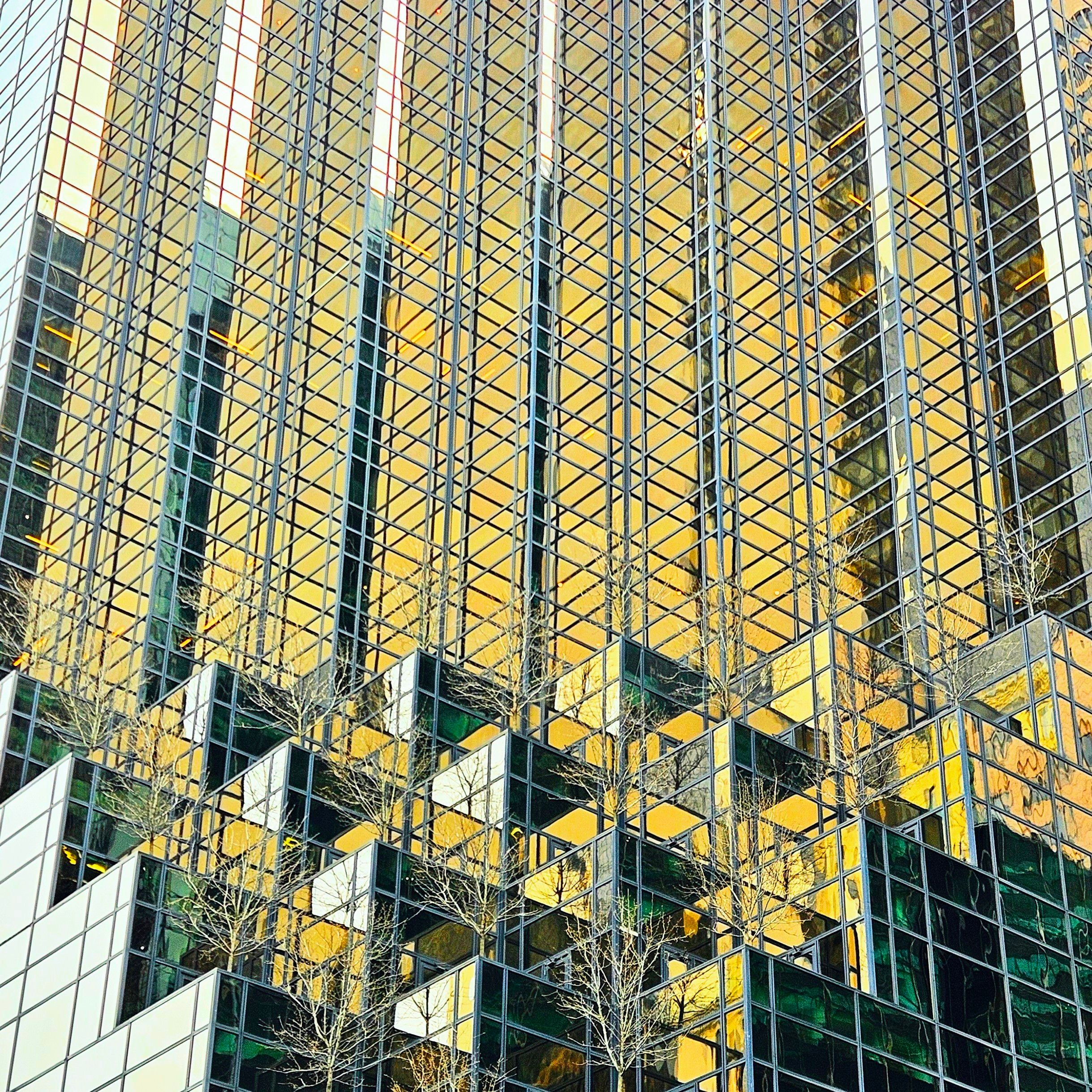 Abstract view of a modern building's glass facade with golden reflections and geometric patterns.