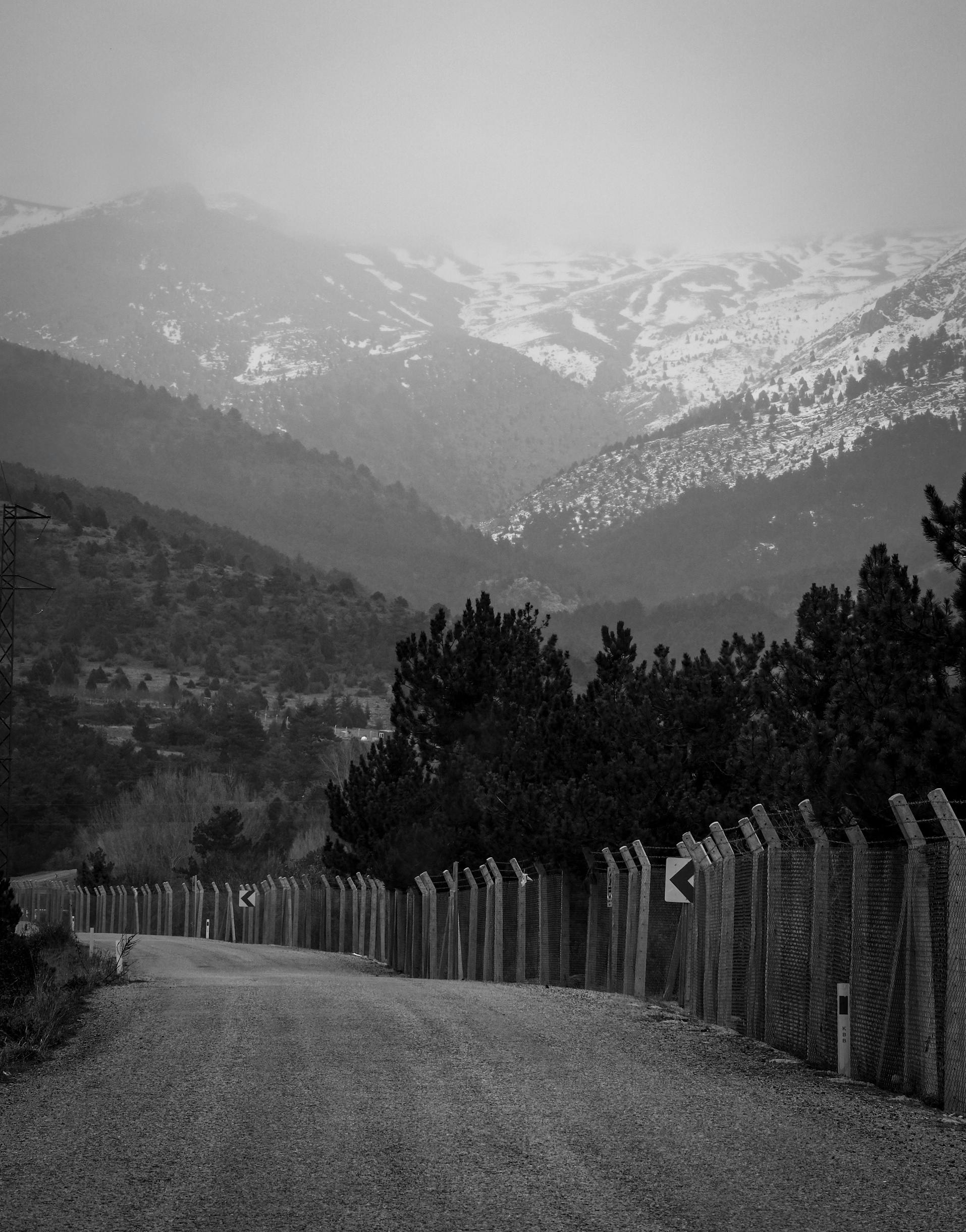Безкоштовне Туманна гірська дорога зі засніженими вершинами та огородженою стежкою чорно-білого кольору. стокове фото