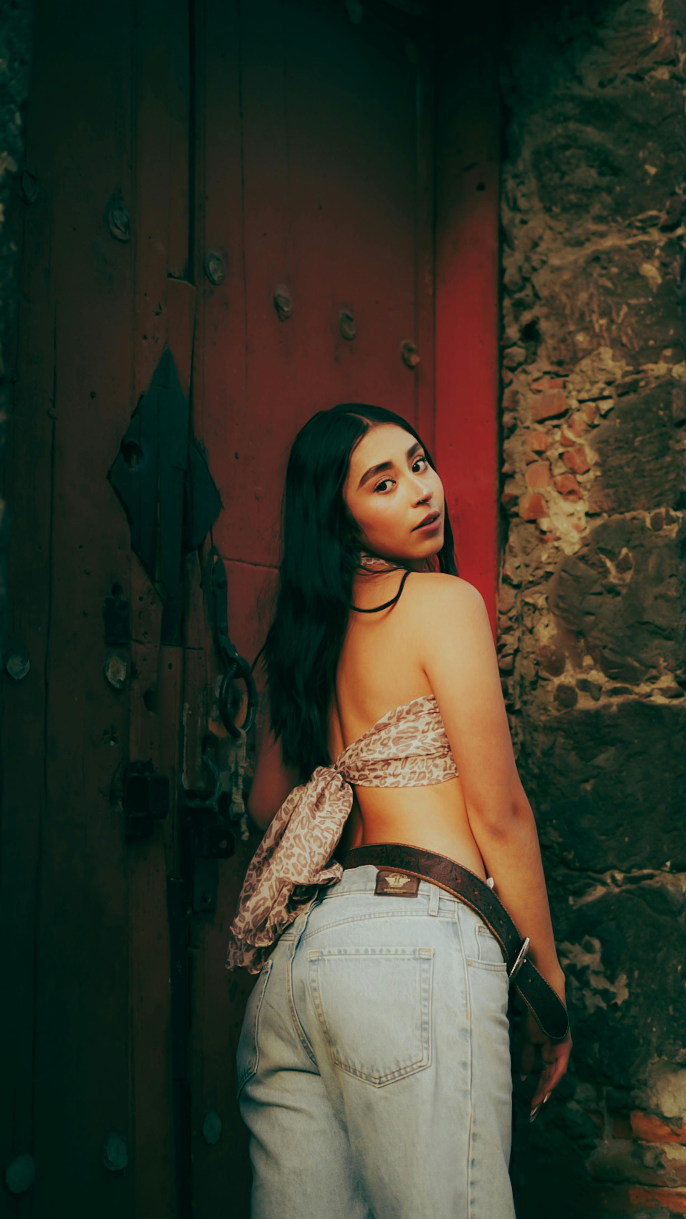 Zadarmo Štýlová mladá žena v ležérnom oblečení pózuje pri rustikálnych dverách opretá o kamennú stenu. Fotka z fotobanky