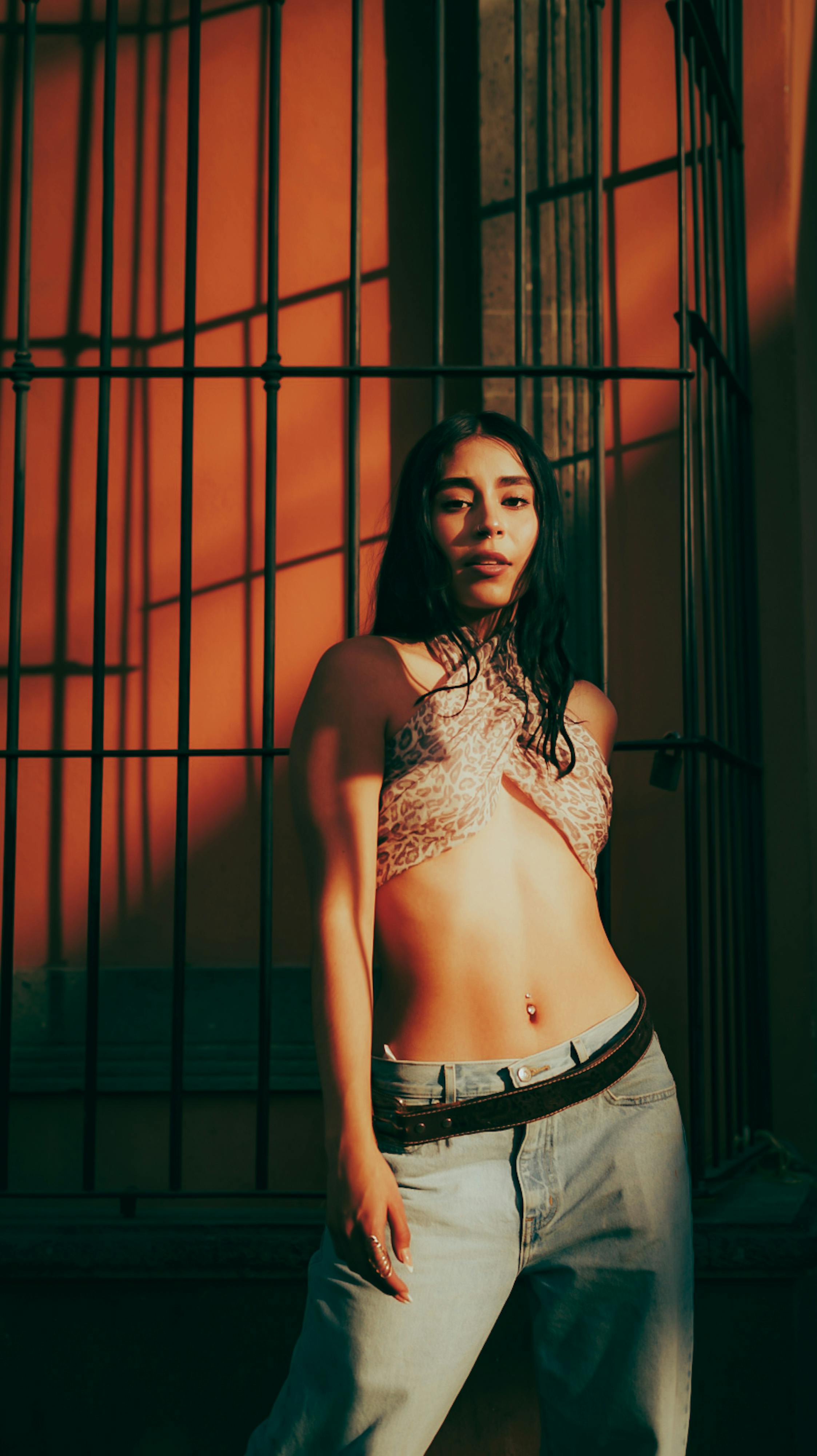 Zadarmo Módna žena sebavedomo pózuje pri železnom plote, zaliata teplým večerným svetlom. Fotka z fotobanky