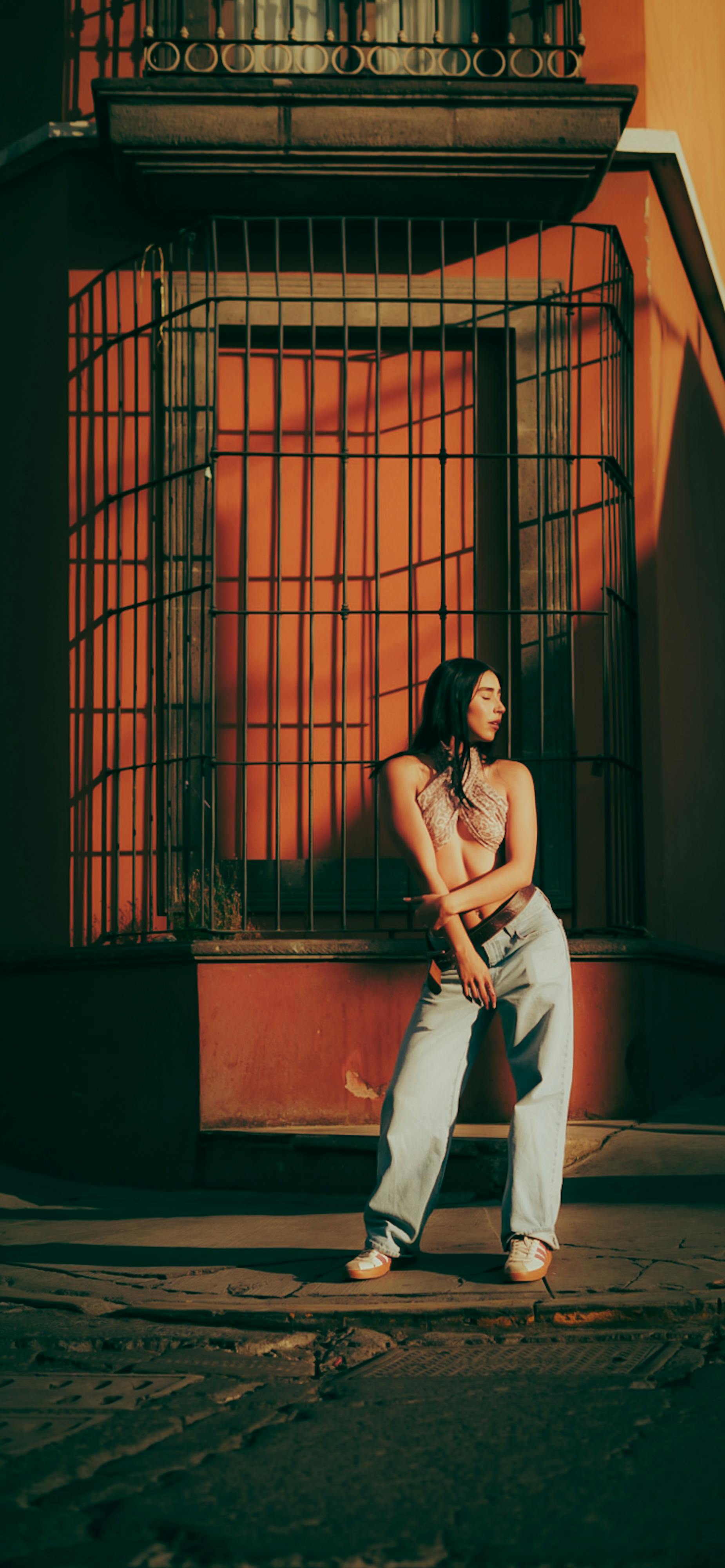ฟรี หญิงสาวทันสมัยคนหนึ่งโพสท่าอยู่หน้าหน้าต่างที่มีลูกกรงในบรรยากาศเมืองช่วงกลางวัน เผยให้เห็นสไตล์สตรีทที่ไม่เหมือนใคร คลังภาพถ่าย