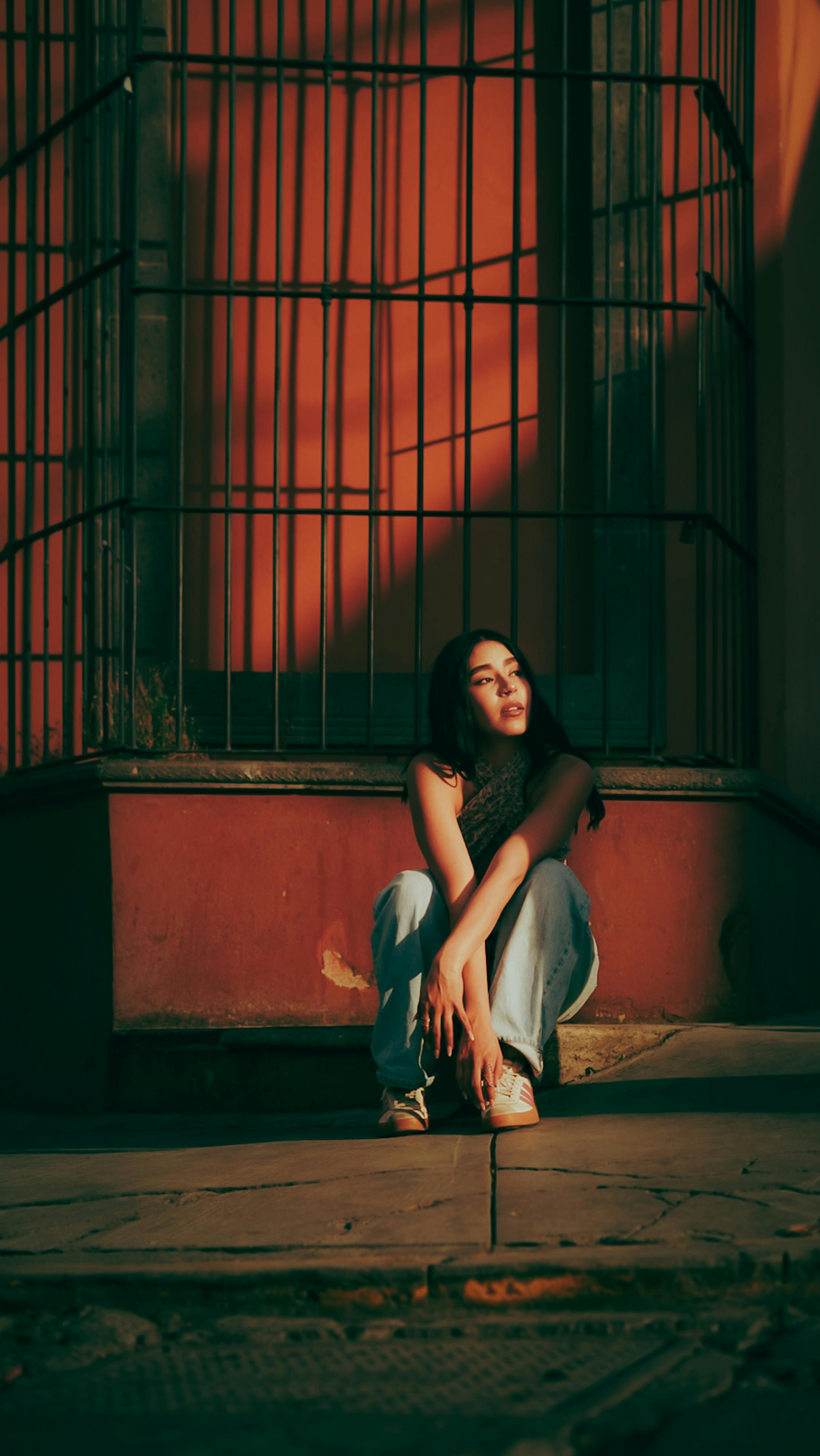 ฟรี หญิงคนหนึ่งนั่งครุ่นคิดอยู่ในบรรยากาศเมืองที่อบอุ่น ท่ามกลางแสงอาทิตย์ยามเย็นที่สาดส่องและเงาที่ทอดยาว คลังภาพถ่าย